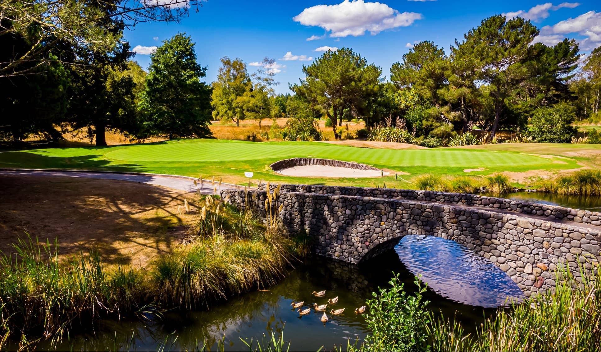 A stone cross bridge with a river running beneath it hugs the edge of the green at the Wairakei Golf Course.