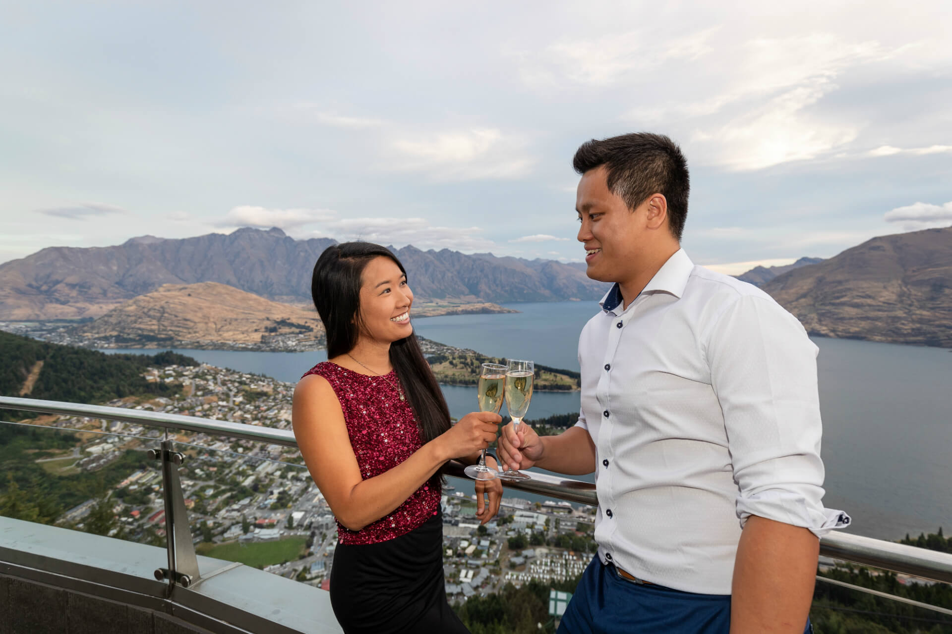A couple on the Skyline Queenstown viewing deck enjoying the view with some champagne.