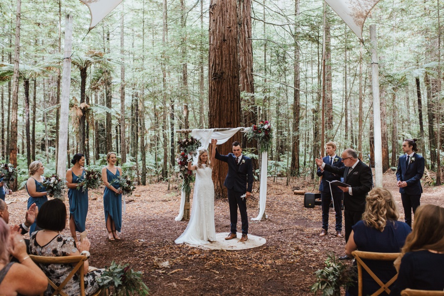 A Bride and Groom raise their hands in the air together celebrating getting hitched.