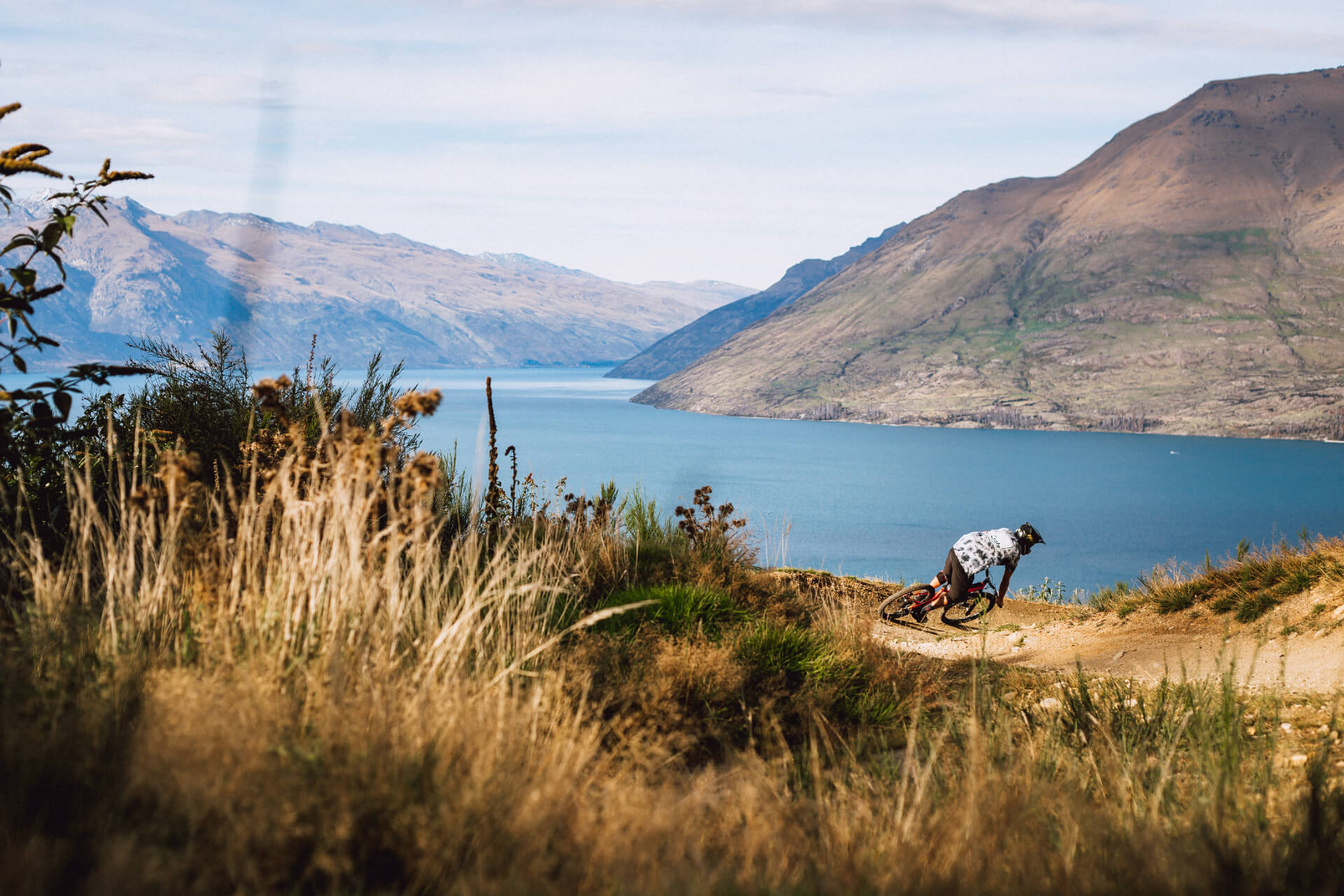 A man rides around a scenic corner in the Skyline Queenstown Bike Park with views of Lake Wakatipu.