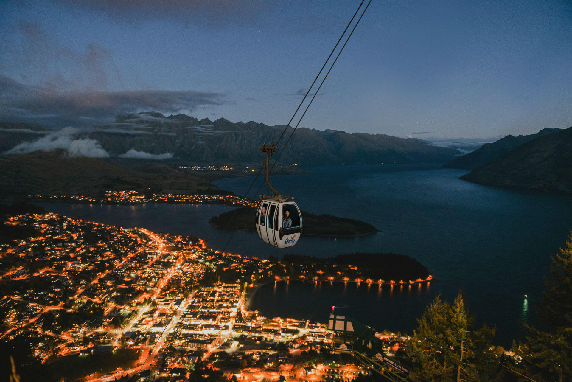 Riding the Skyline Queenstown Gondola just after sunset with the lights of Queenstown in the background.