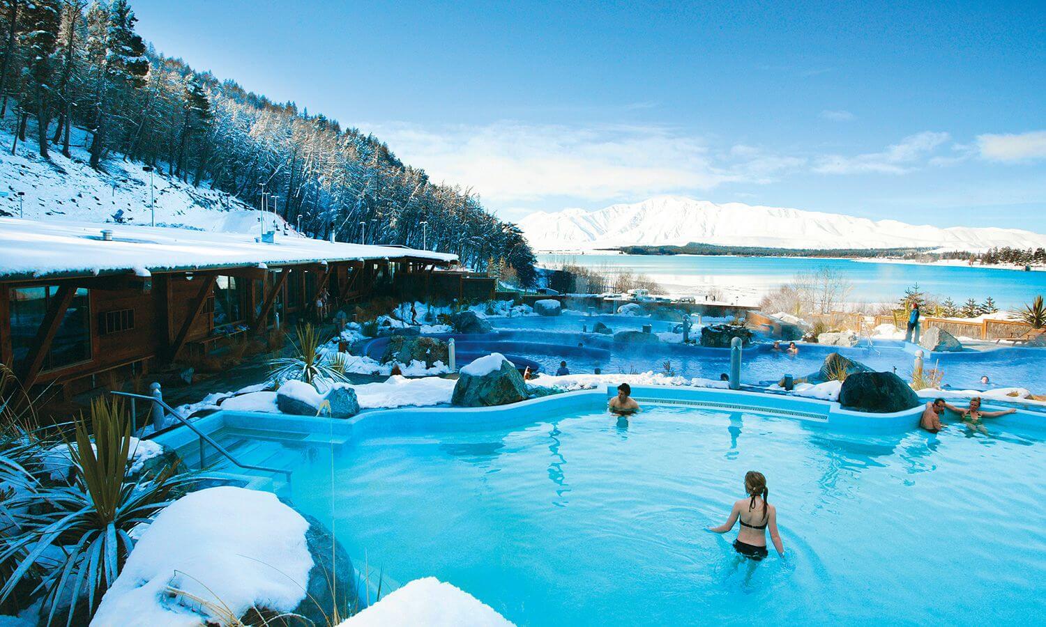Vibrant blue pools surrounded by snow under a blue sky at Tekapo Springs.