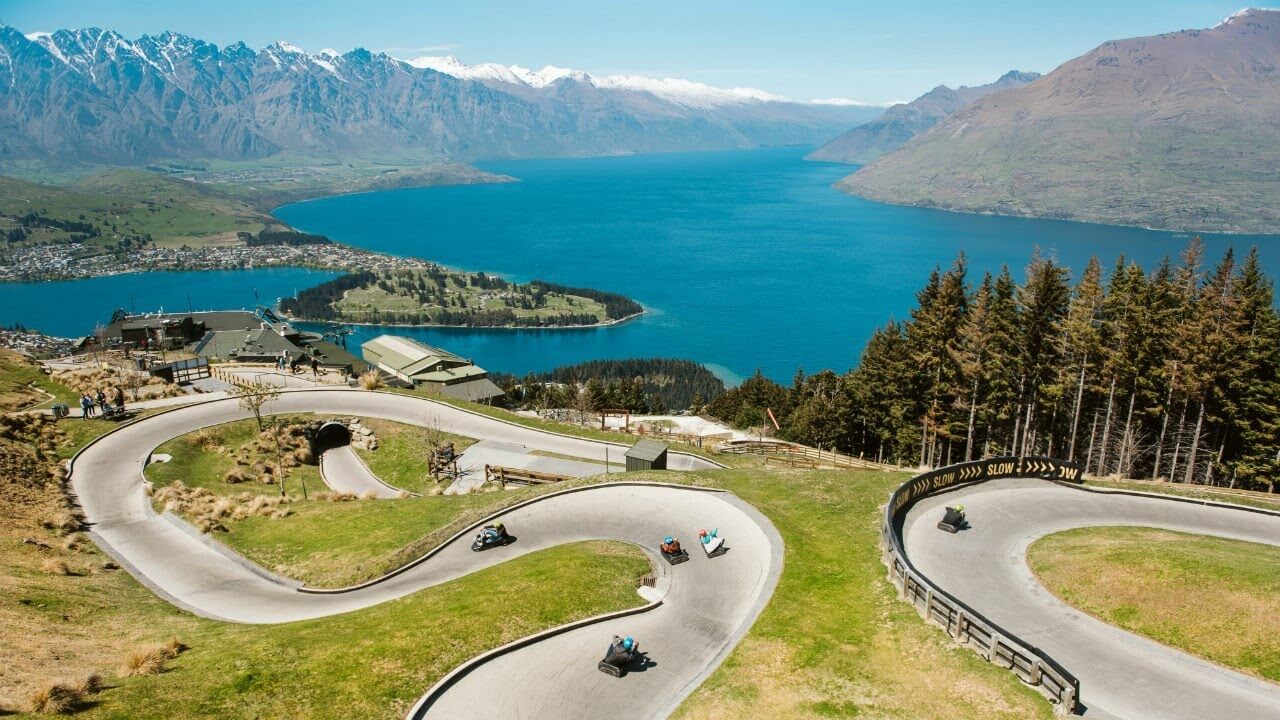 A longshot of the luge tracks at Skyline Queenstown that riders going down the luge while overlooking the lake and mountains.