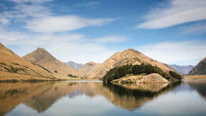 Moke Lake with mountains in the background under a blue sky with scattered clouds.
