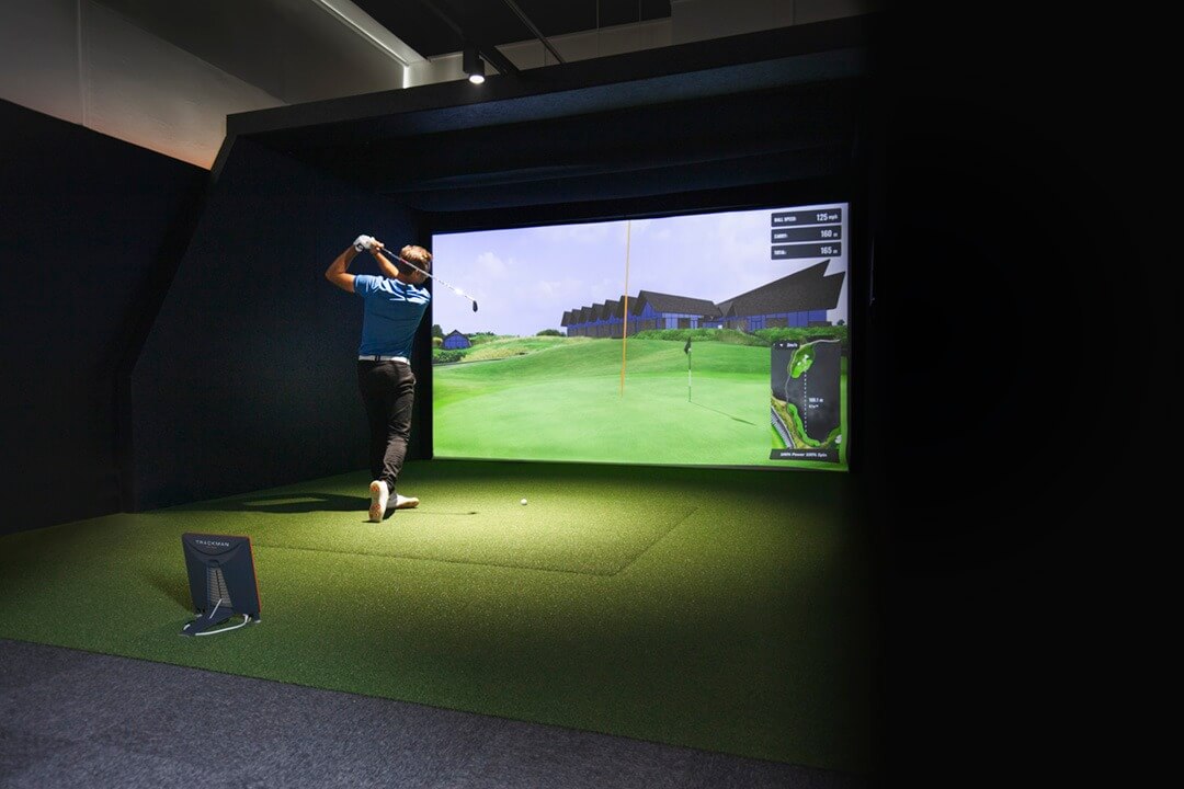 A man swings his club and hits a ball at an indoor golf simulator.