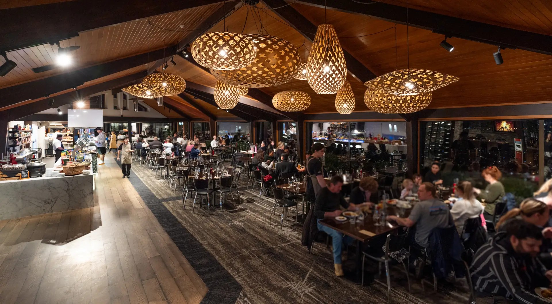 The interior of a large buffet restaurant with many tables of customers eating under uniquely shaped chandeliers.