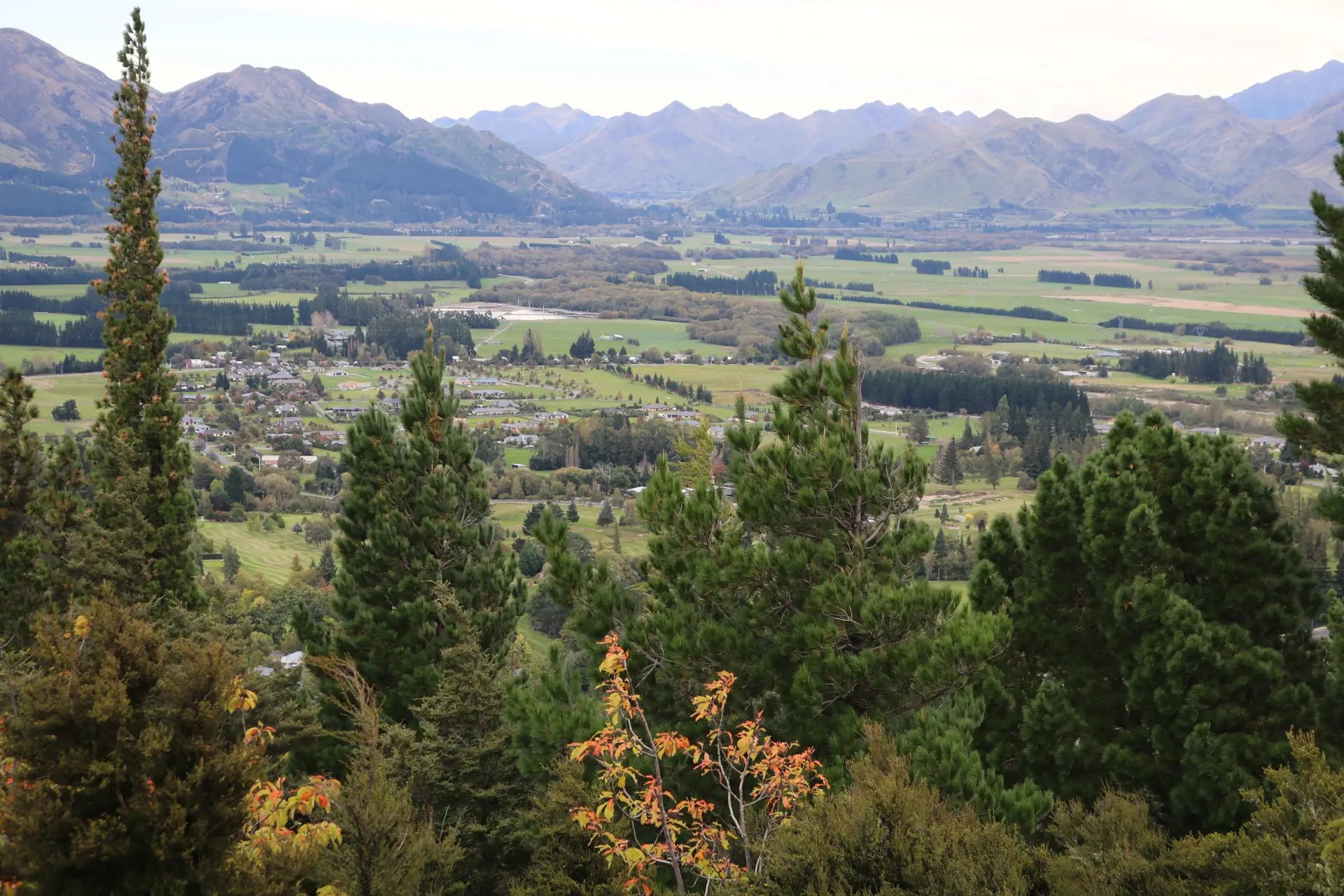 View from Conical Hill overlooking Hanmer Springs town with green plains and mountain ranges in the distance.
