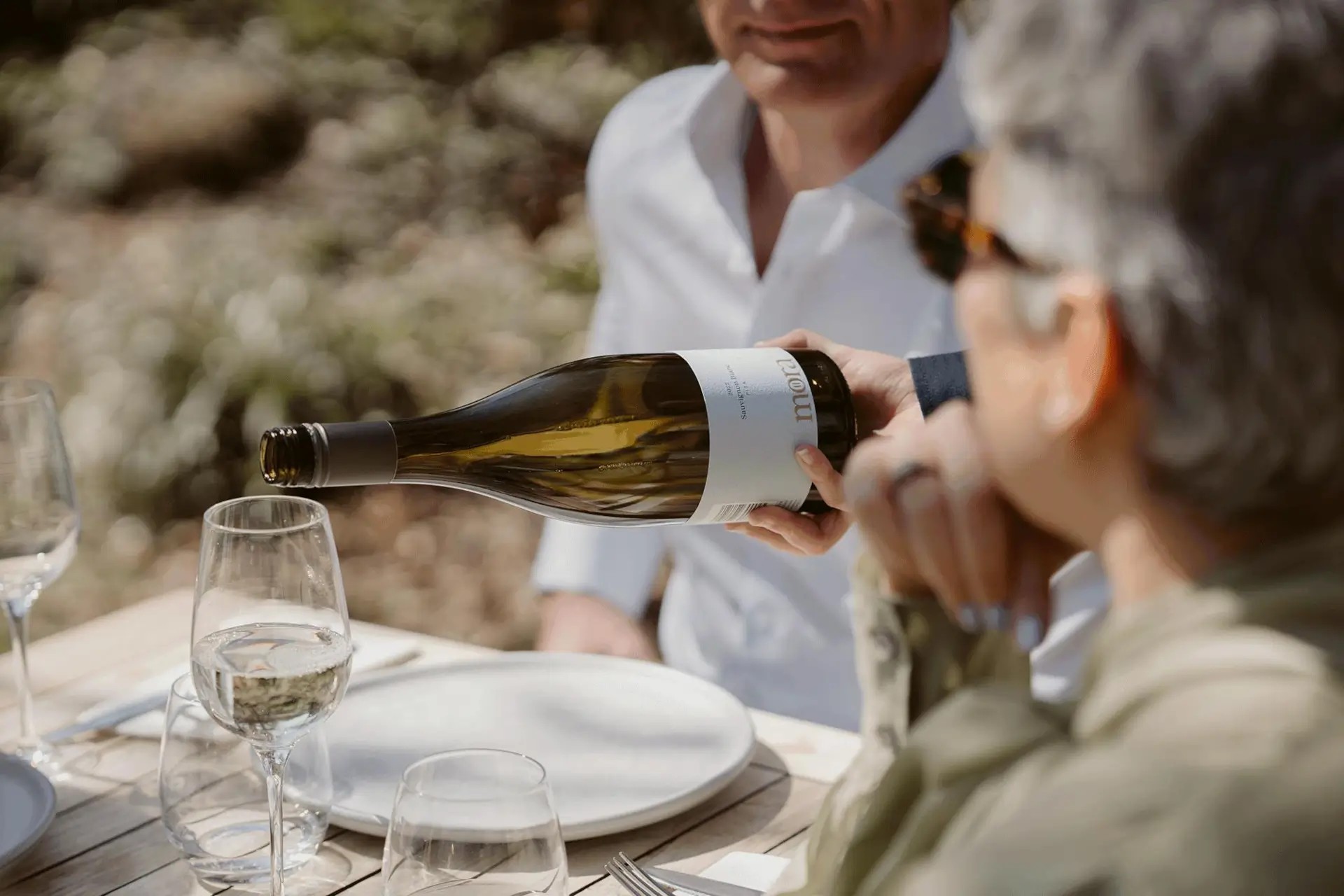 Person pouring sauvignon blanc wine for two guests.