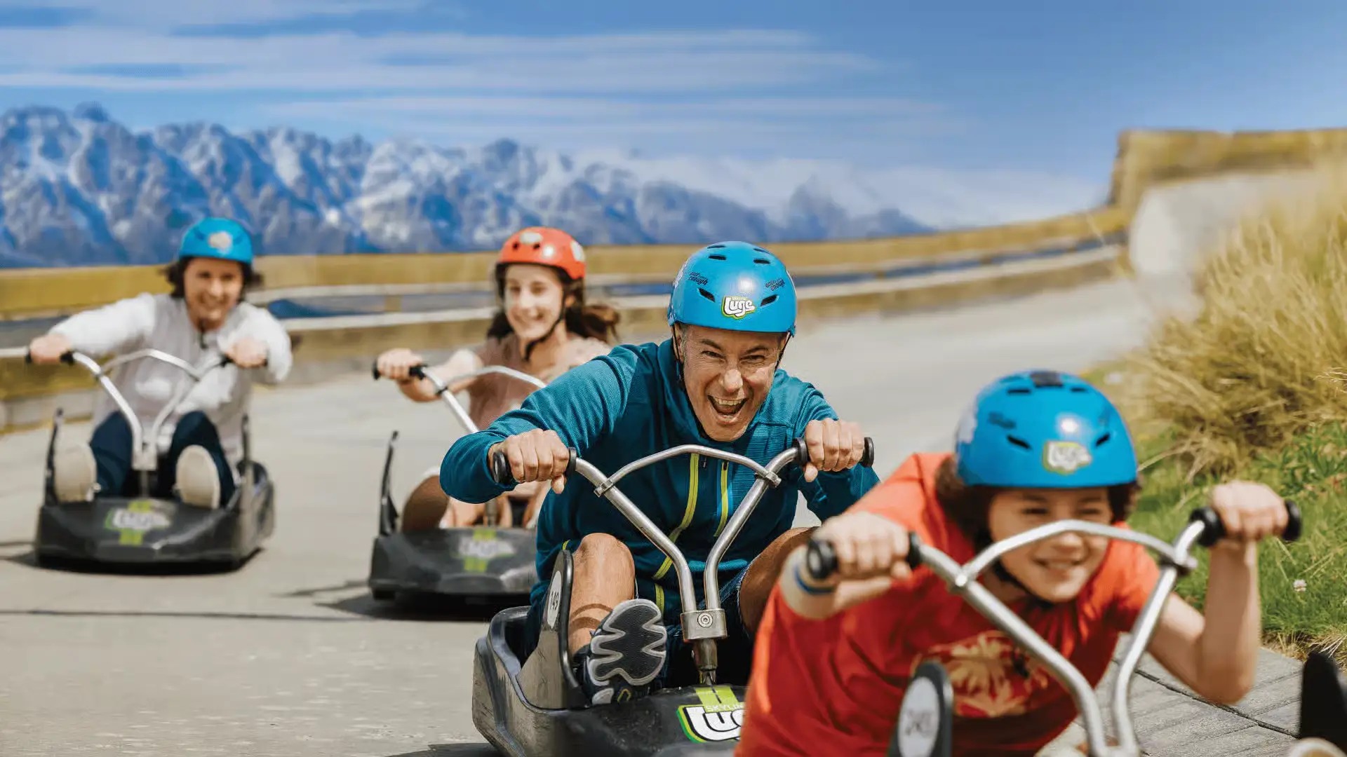 Four luge riders excitedly going down a trail at Skyline Queenstown.