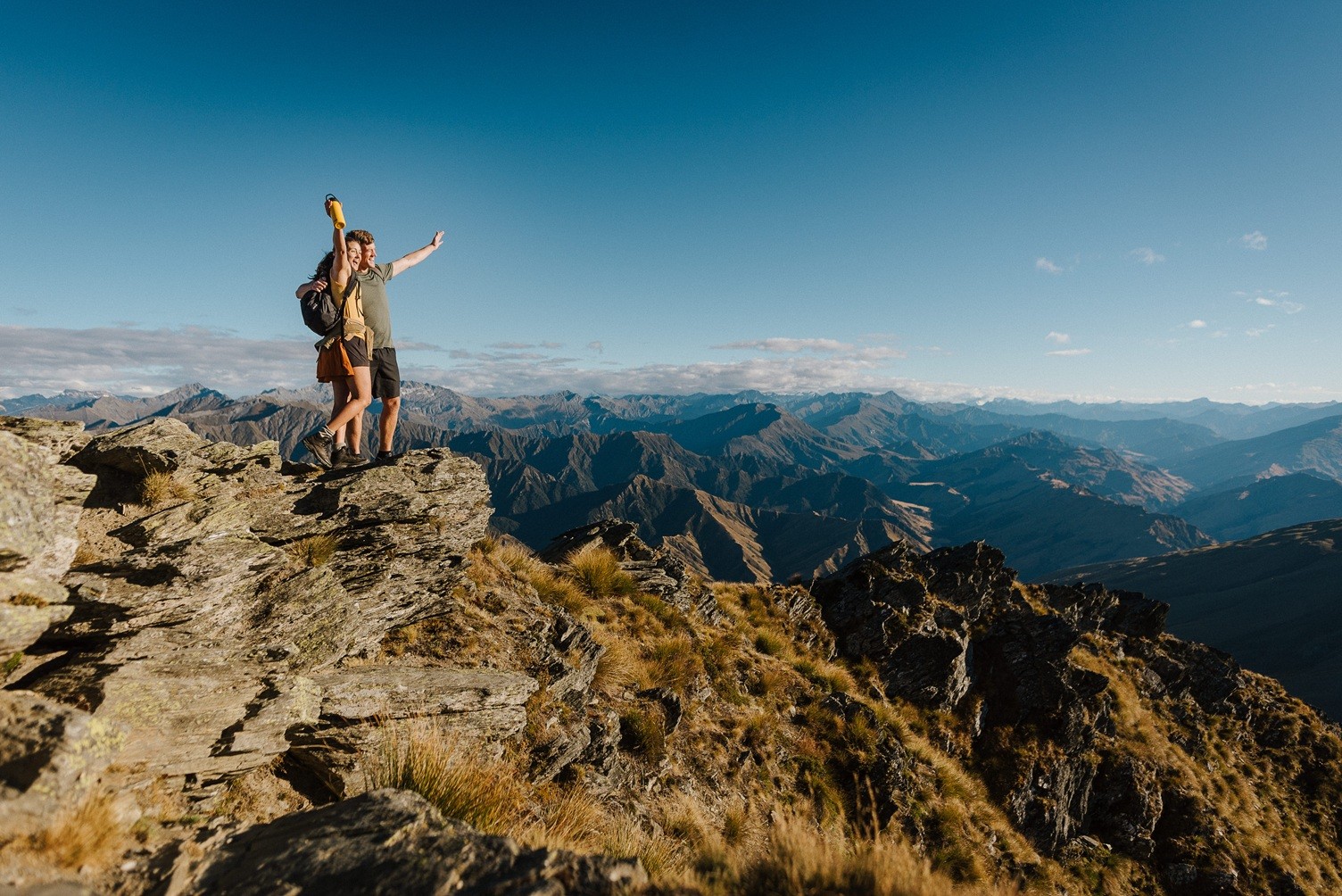 Two friends throw their arms in the air to celebrate reaching the top of Ben Lomond mountain peak.