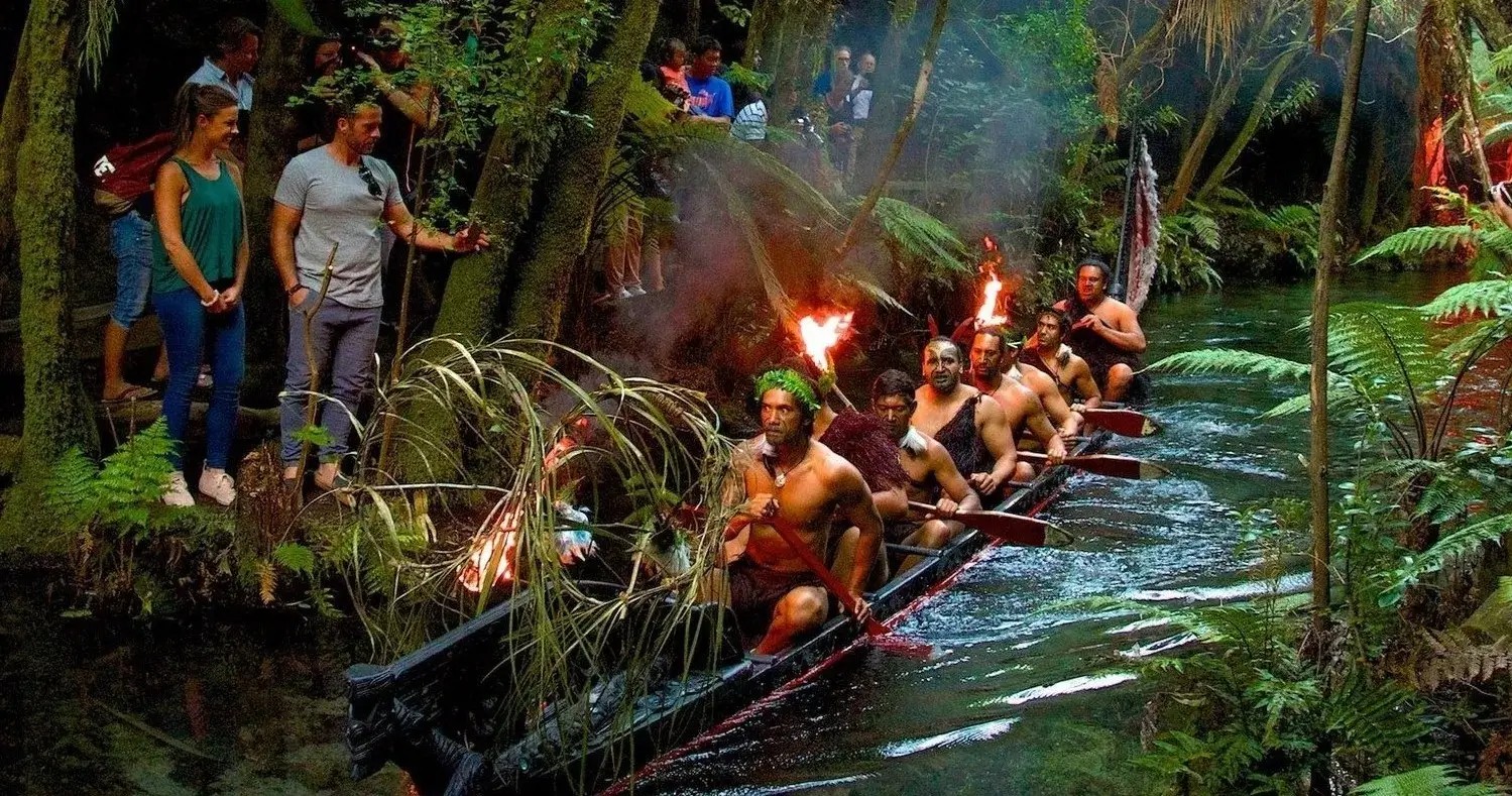 A group of men rowing a waka in a forest at the Mitai Maori Village experience in Rotorua.