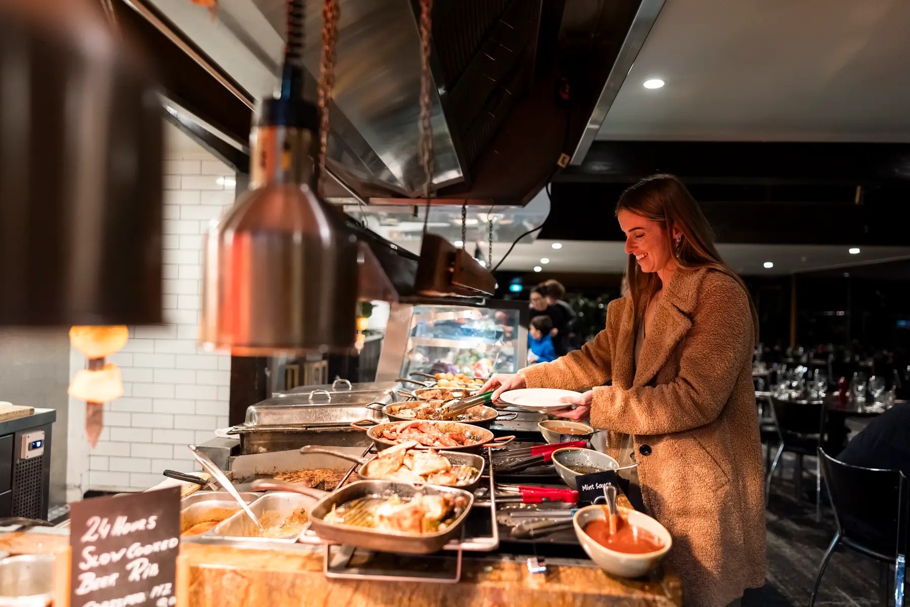 A woman picking up food with tongs at the Stratosfare Restaurant buffet in Rotorua at night.