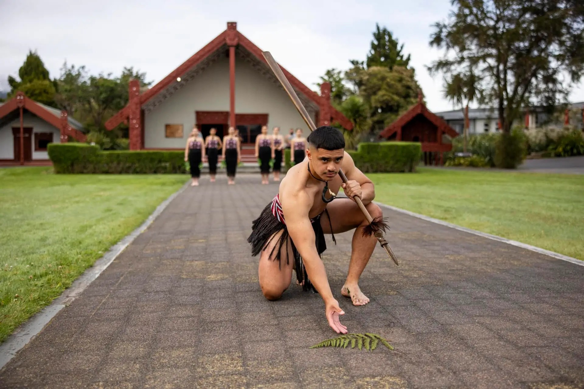 A man performing in front of a group of women and a marae at Te Puia, Rotorua.