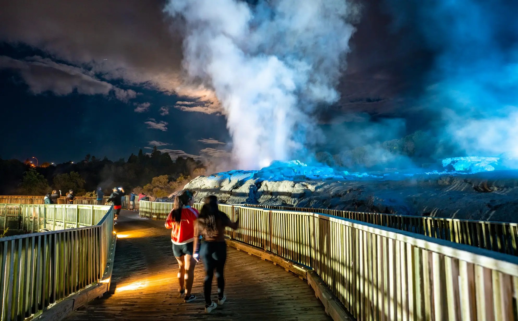 Visitors walking down a broadwalk and looking at a geyser at Te Puia, Rotorua.