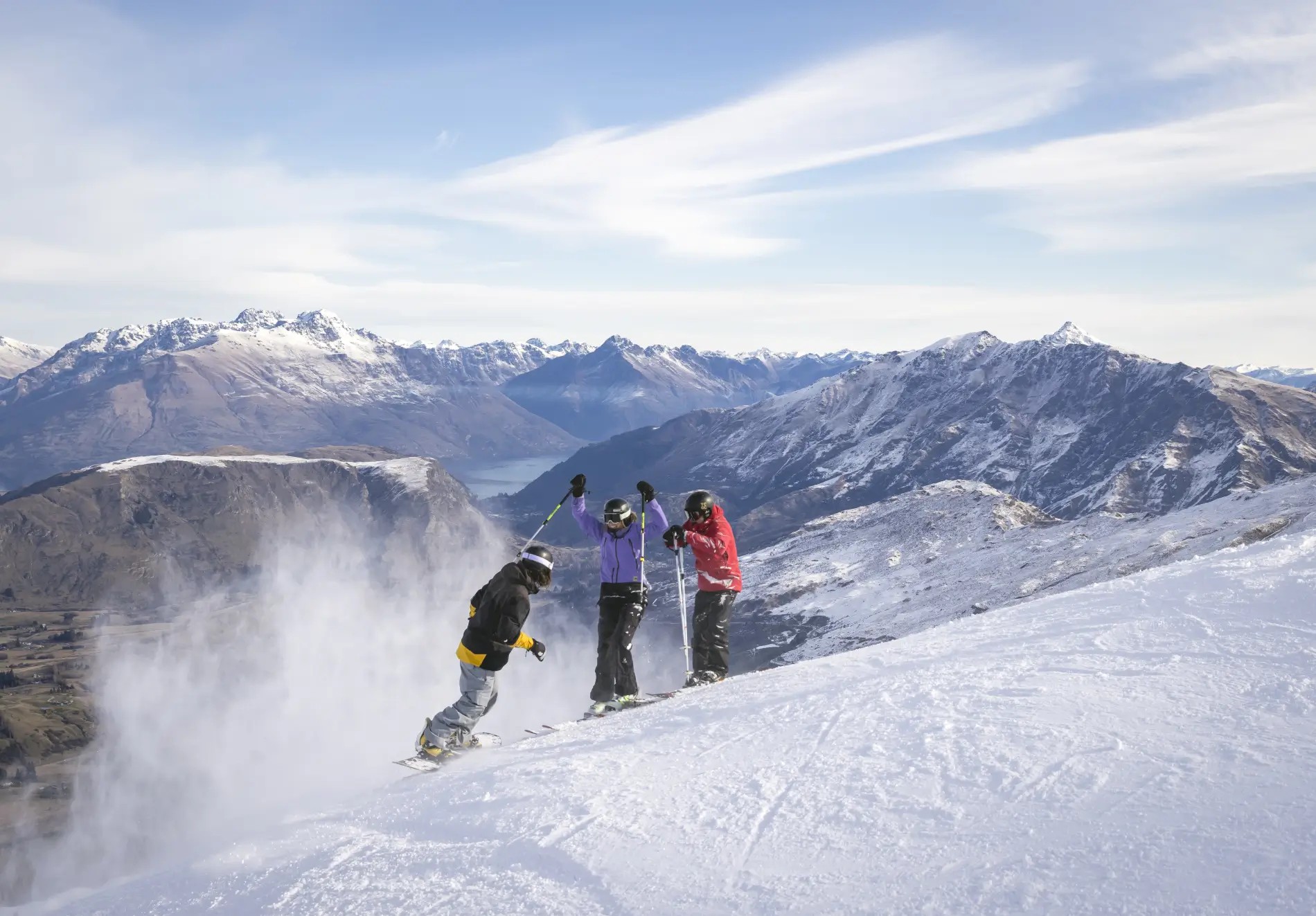 Two skiers and one snowboarder standing on the snow in the Coronet Peak ski field, Queenstown.
