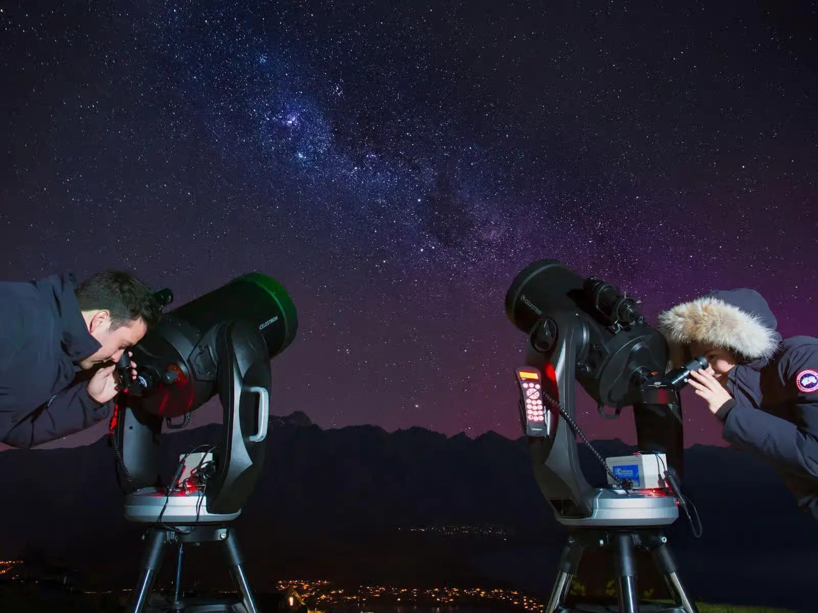 Two people each looking through a telescope at the night sky in Queenstown.