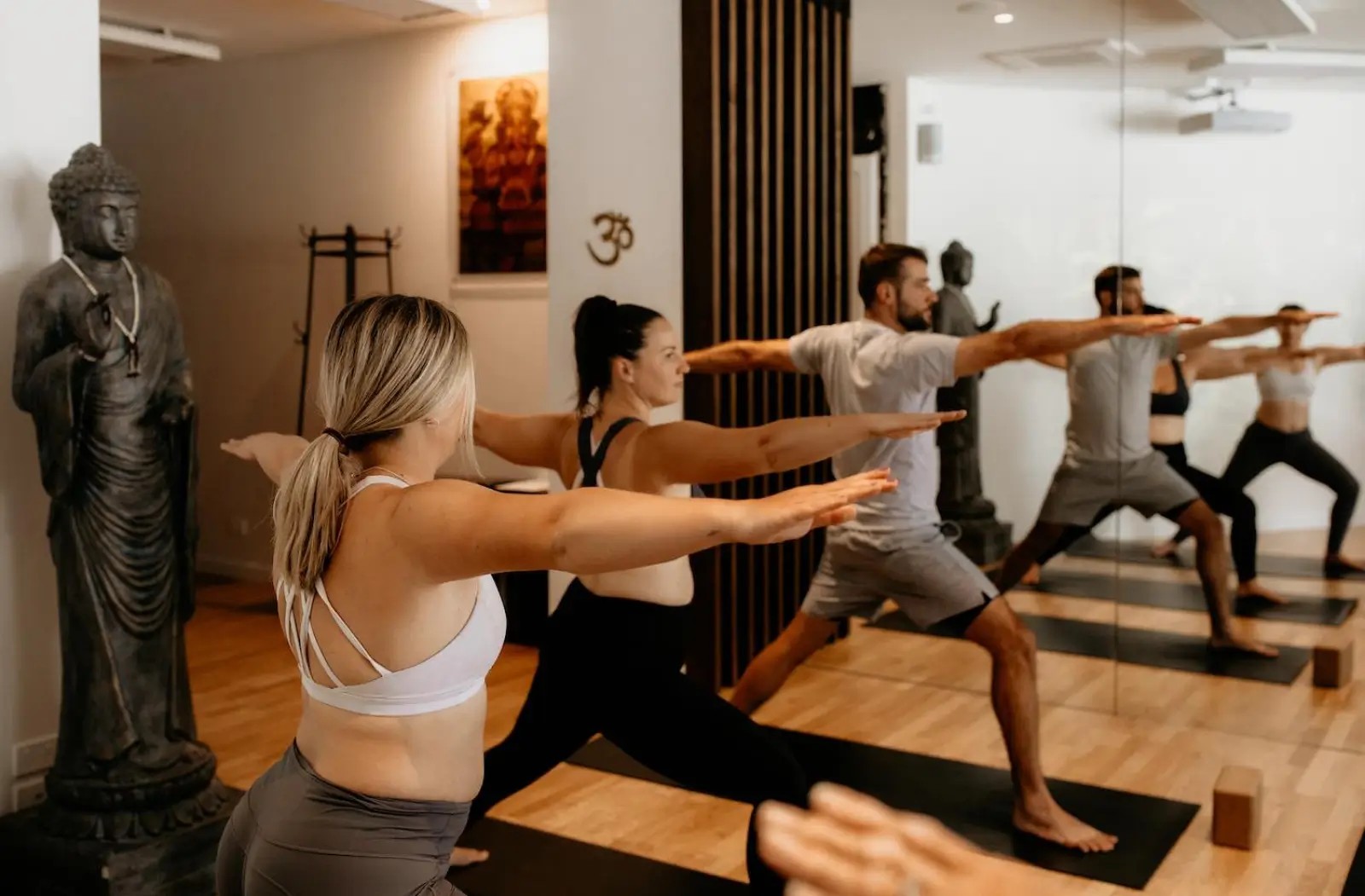 Three people doing a yoga pose in front of a mirror.