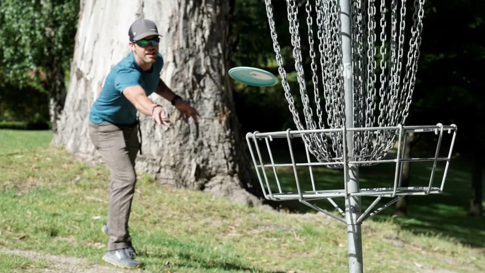 Man throwing a frisbee into a disc golf basket in the Queenstown Gardens.