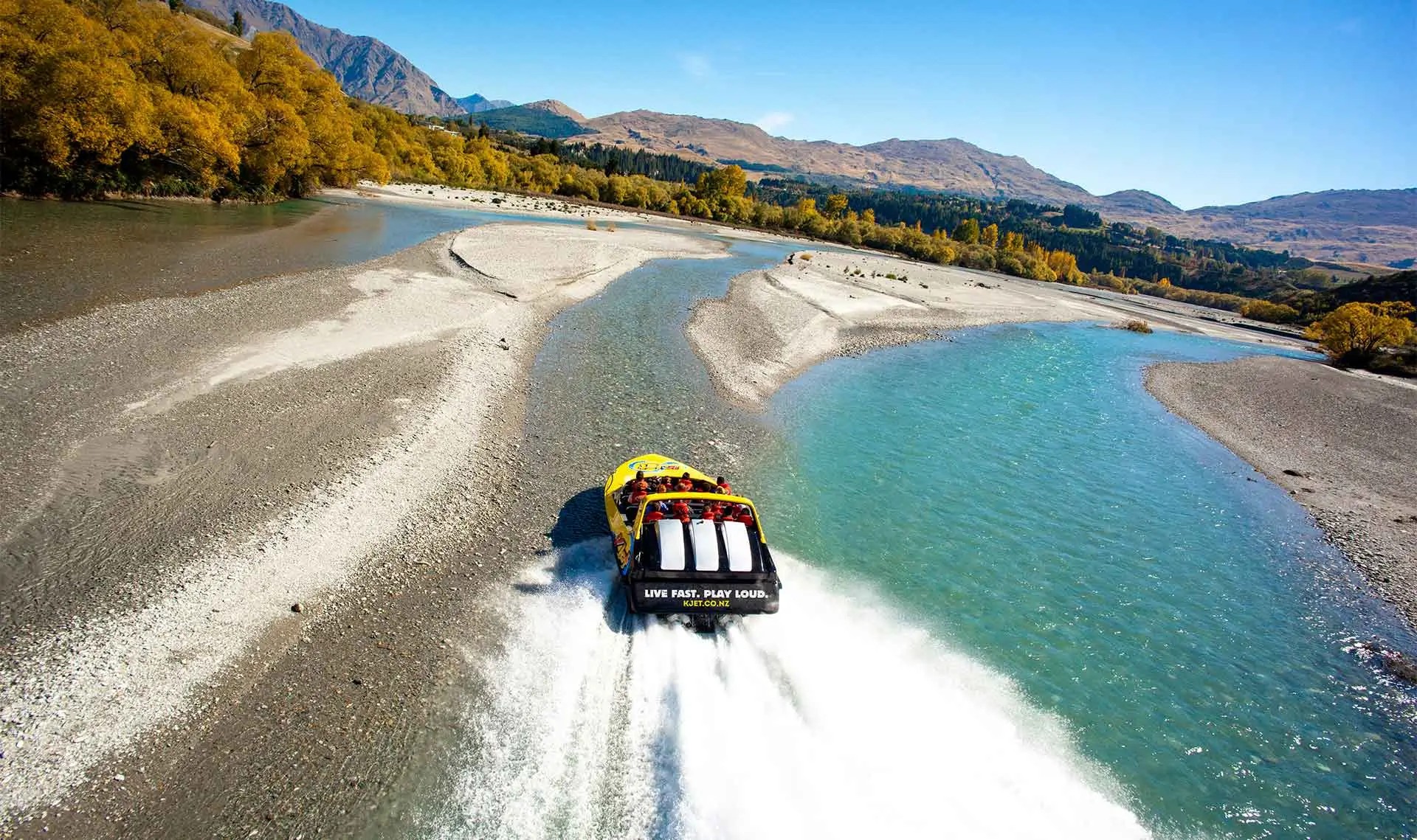 KJet jet boat gliding over the braided sand and water of the Shotover River.