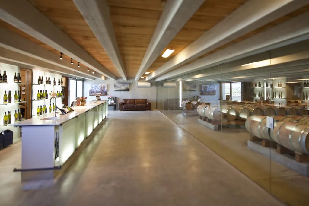 Contemporary wine cellar featuring oak barrels, tasting counter with bottles, exposed timber beams and lounge space.