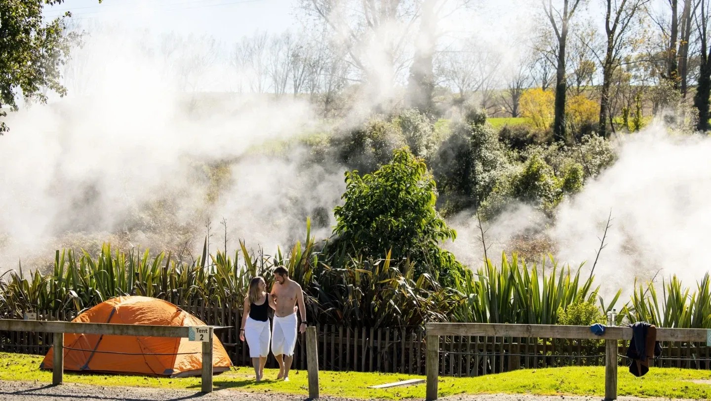 Thermal camping area featuring tent accommodation, steam from natural springs and guests enjoying facilities.