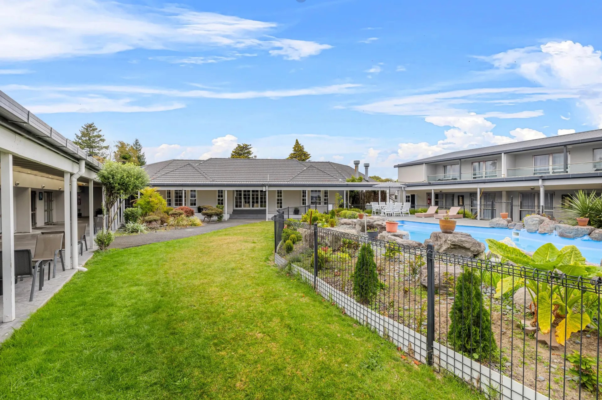 Spa resort grounds with fenced pool area, green lawns, palm plantings and modern accommodation buildings.