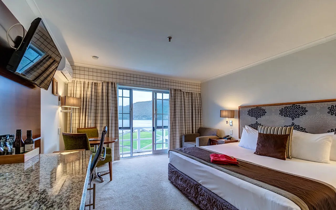 Lakefront hotel room with scenic views, elegant bedding, writing desk and stylish interior design elements.