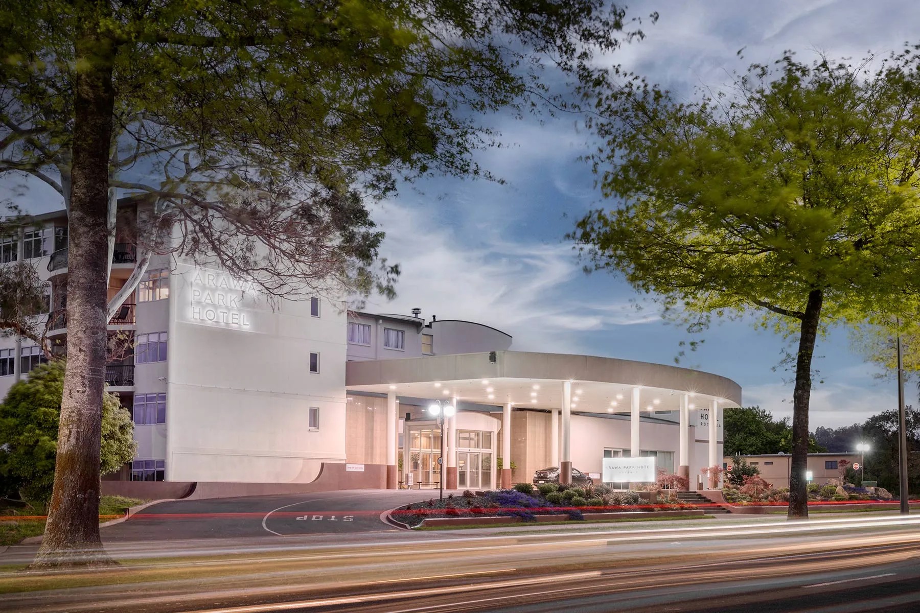 Arawa Park Hotel exterior at twilight with curved entrance canopy, illuminated signage and landscaped gardens.