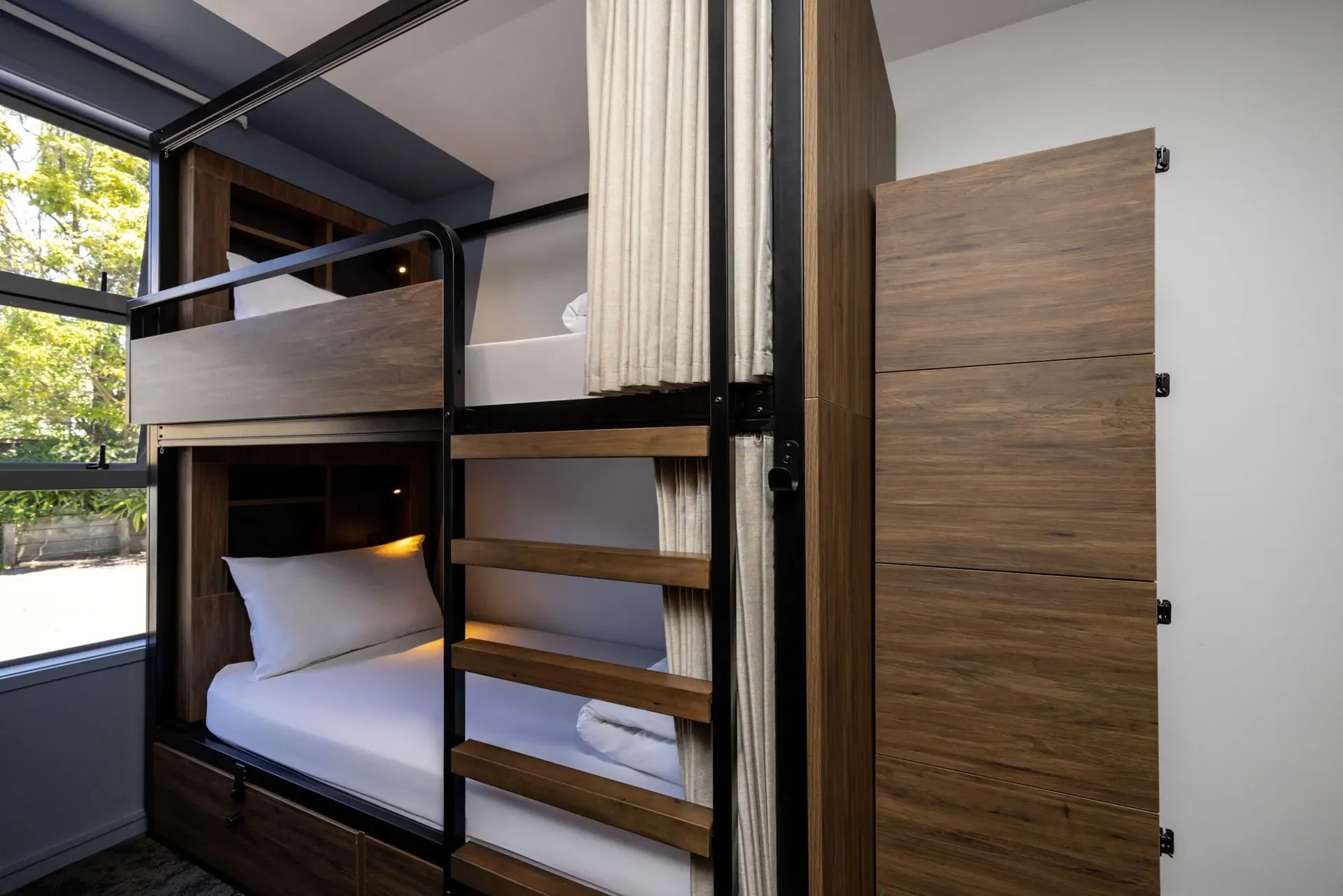 Stylish shared accommodation with wooden bunk beds, white linens, privacy screens and storage compartments.