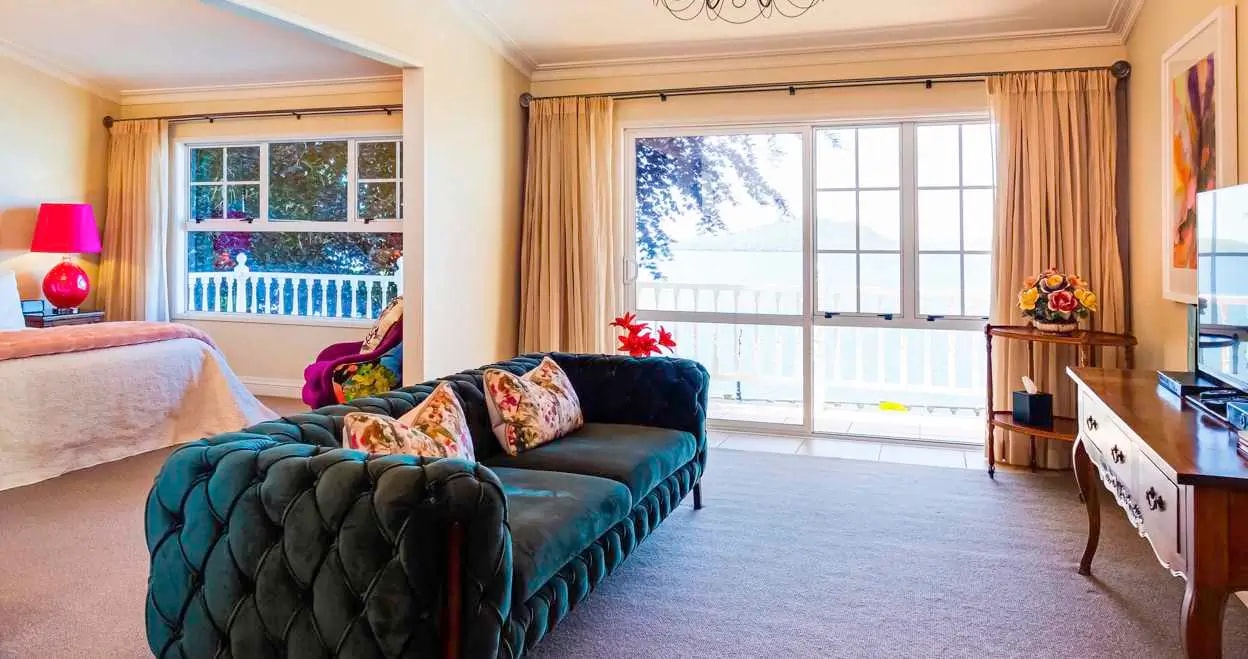 Elegant hotel suite with teal velvet sofa, floral cushions, lake view windows, partial bed view and classic furnishings.