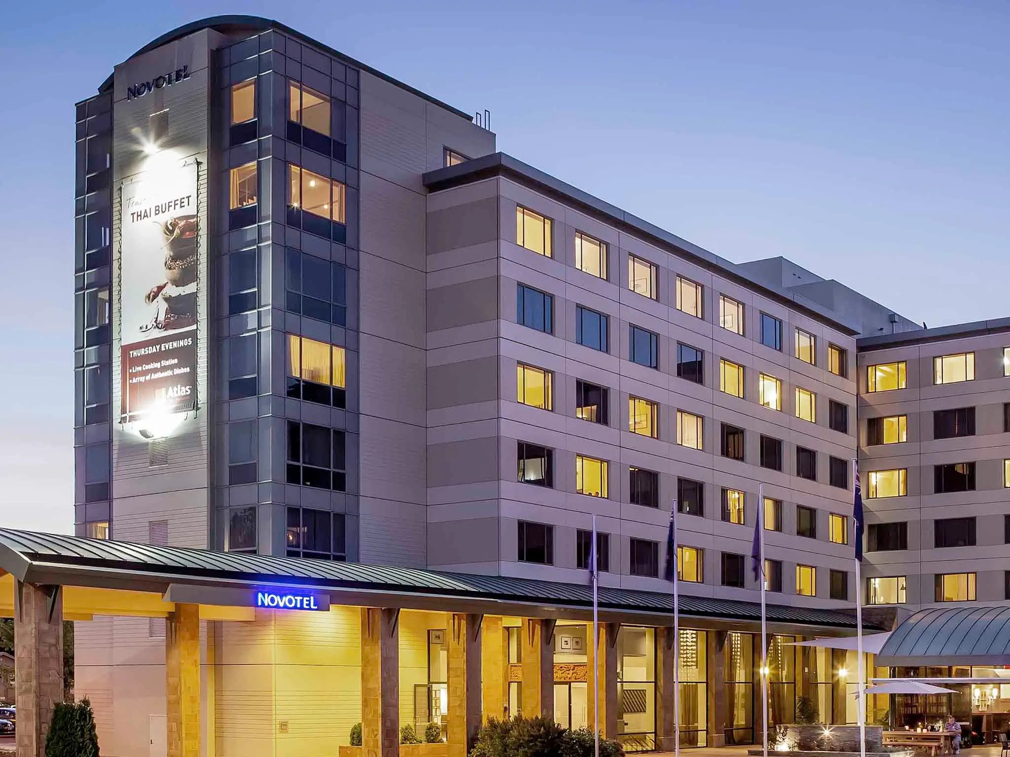 Contemporary hotel facade during evening hours with bright entrance lighting and illuminated guest room windows.