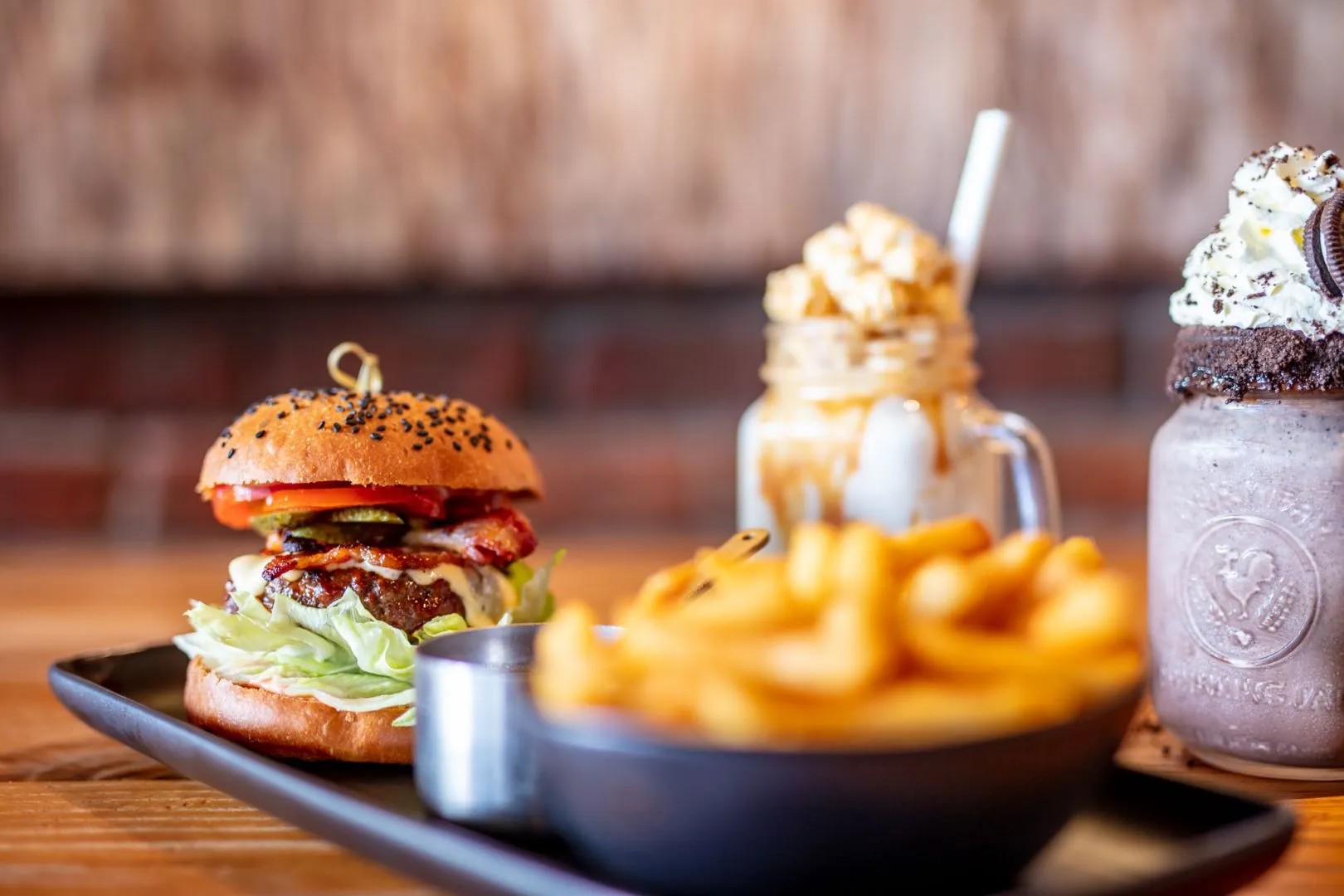 Small beef burger, sauce, and fries on a black plate, accompanied by an iced chocolate and caramel drink.