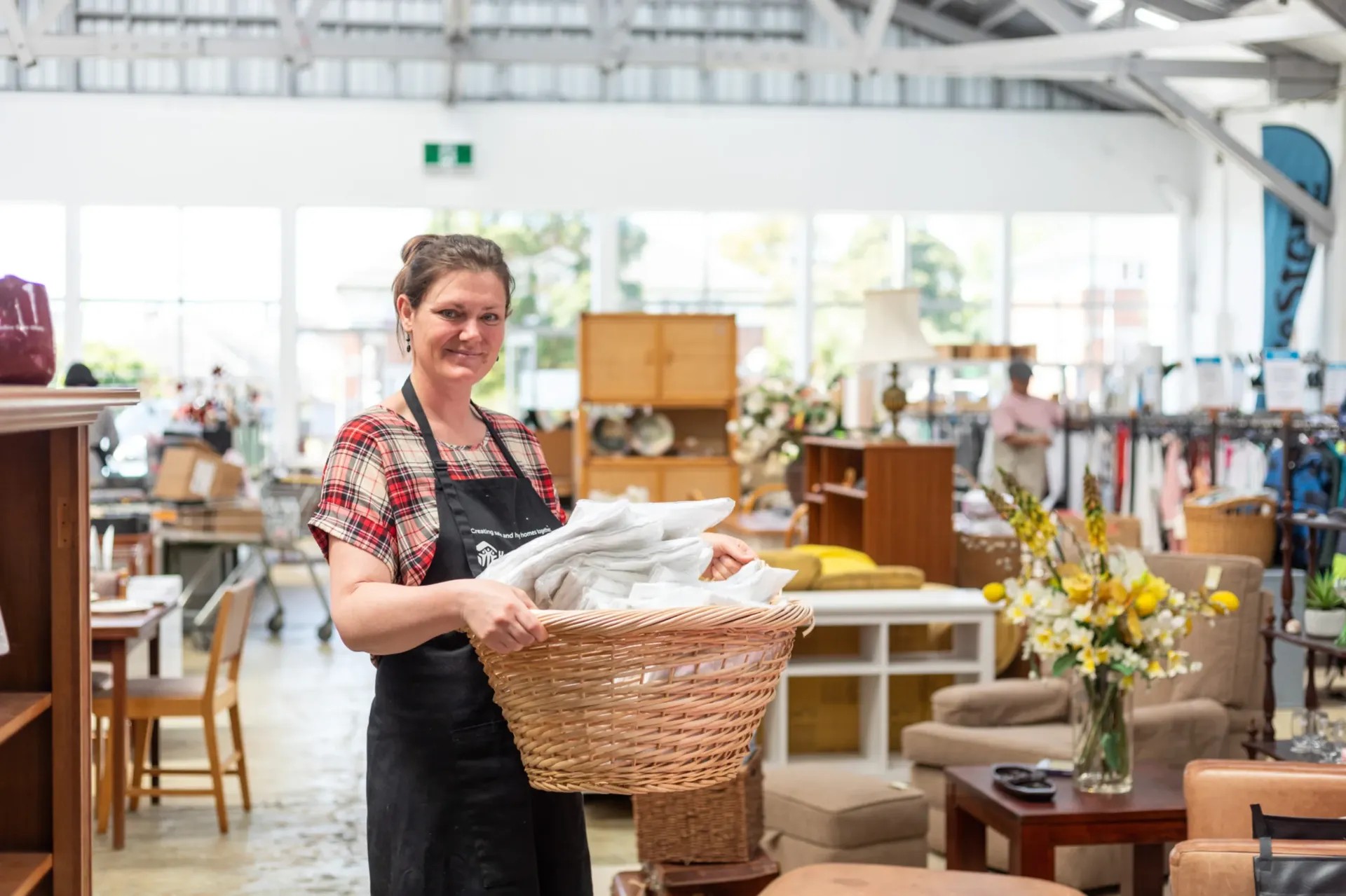 Woman holding a basket of towels inside a large op shop.