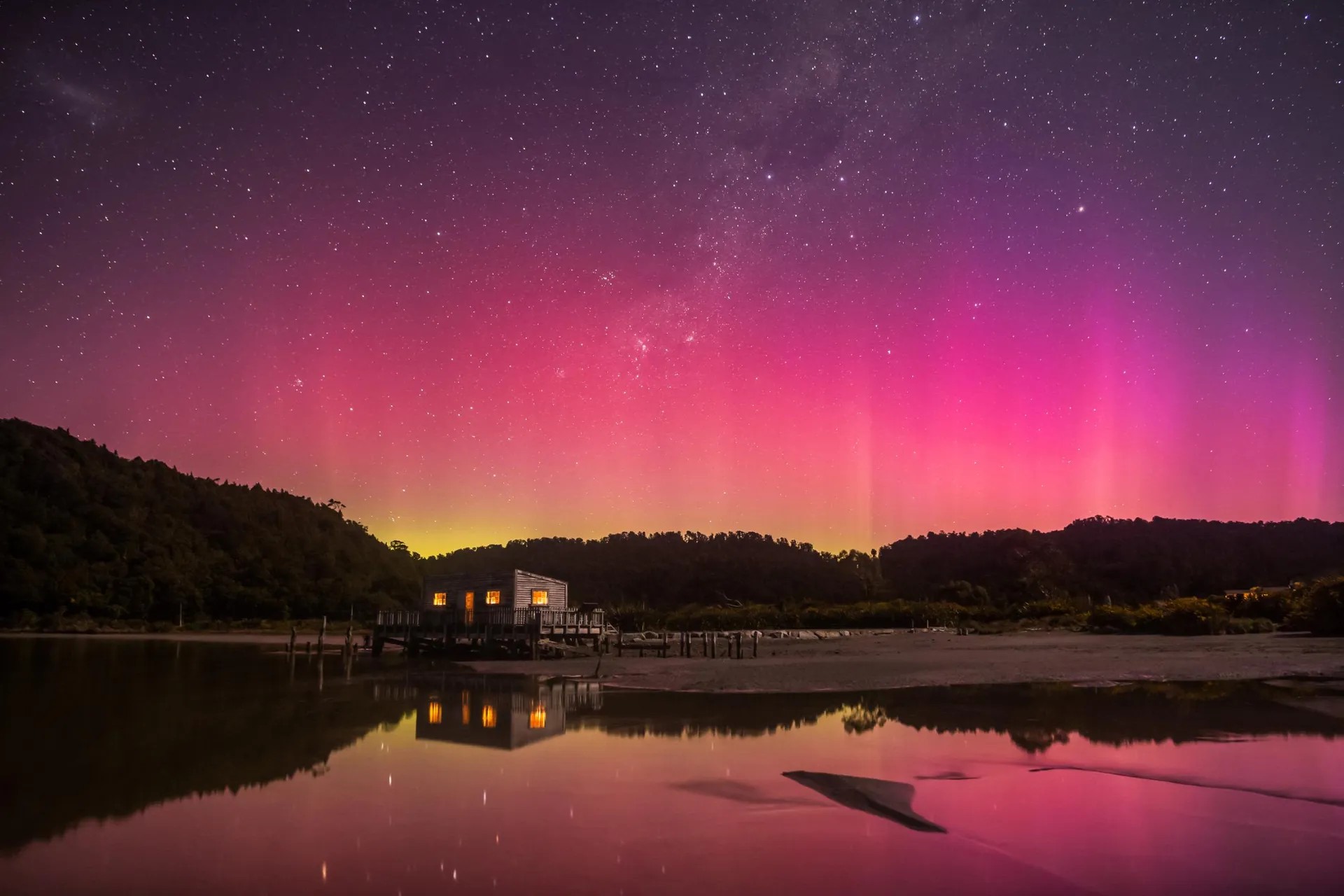 Beautiful pink, purple and yellow Southern Lights in Okarito with a wooden building.