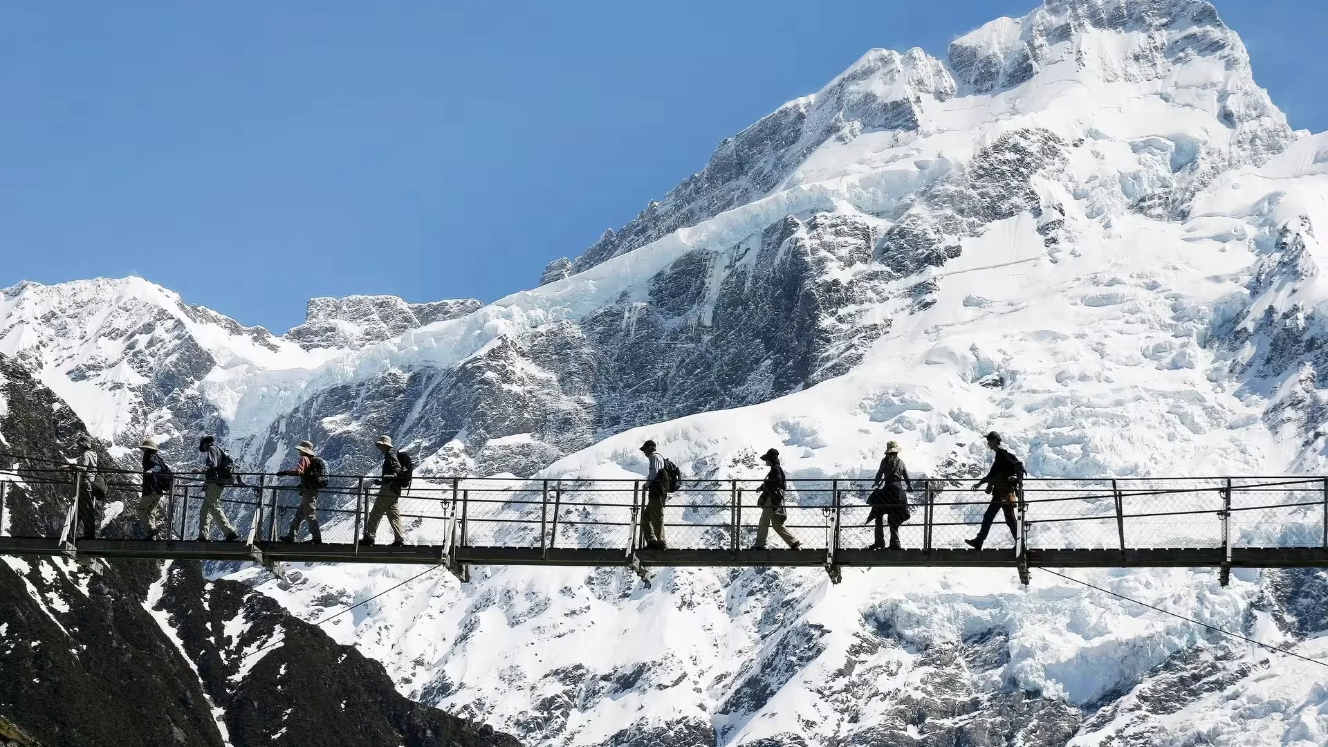 Group of hikers walking on a suspension bridge on snowy Mount Gunn.