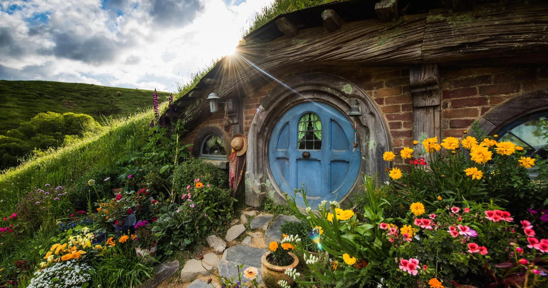 Hobbiton home with blue door and colorful flowers surrounding it.