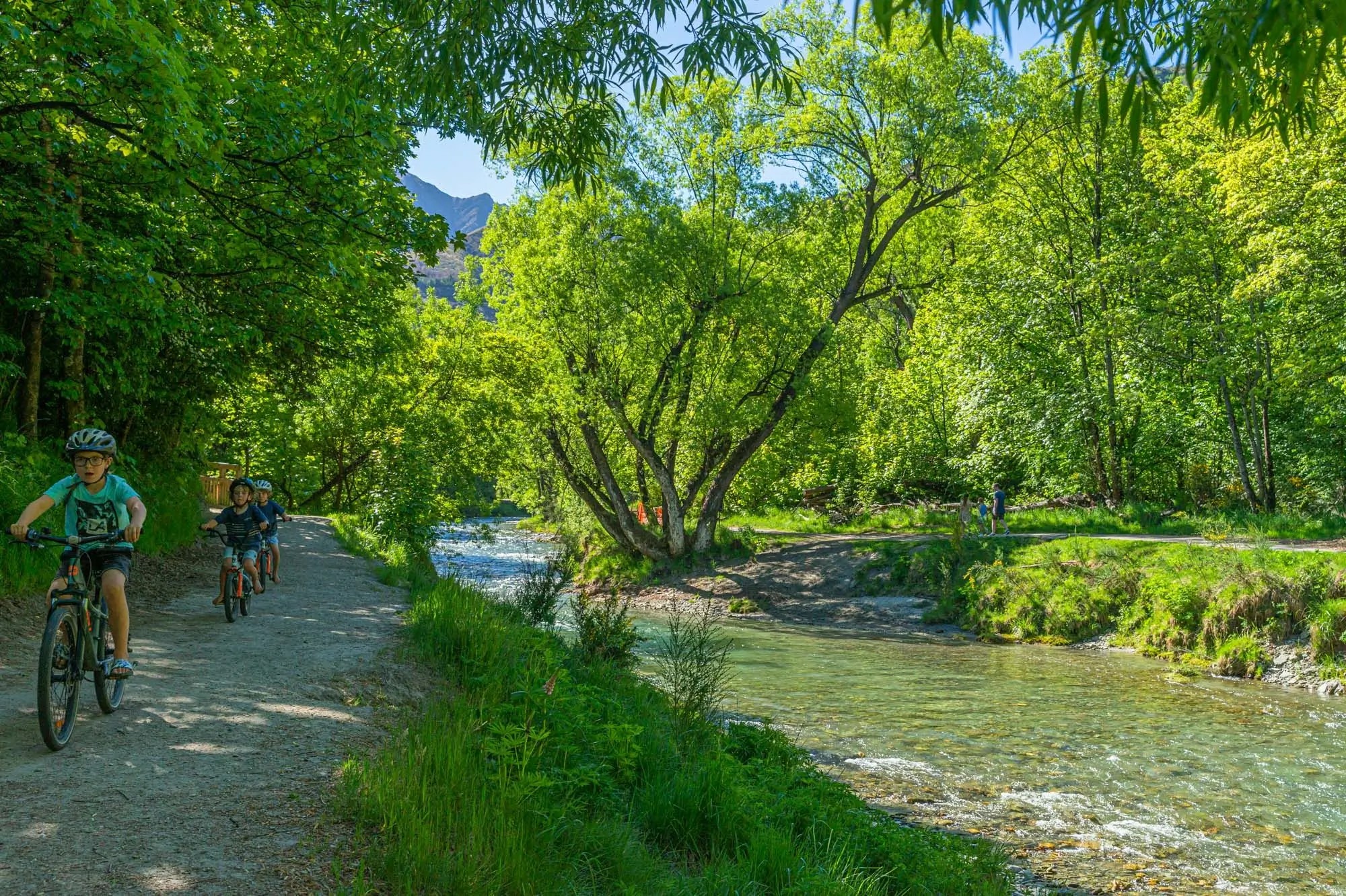 Kids biking along Arrow River on a sunny day.