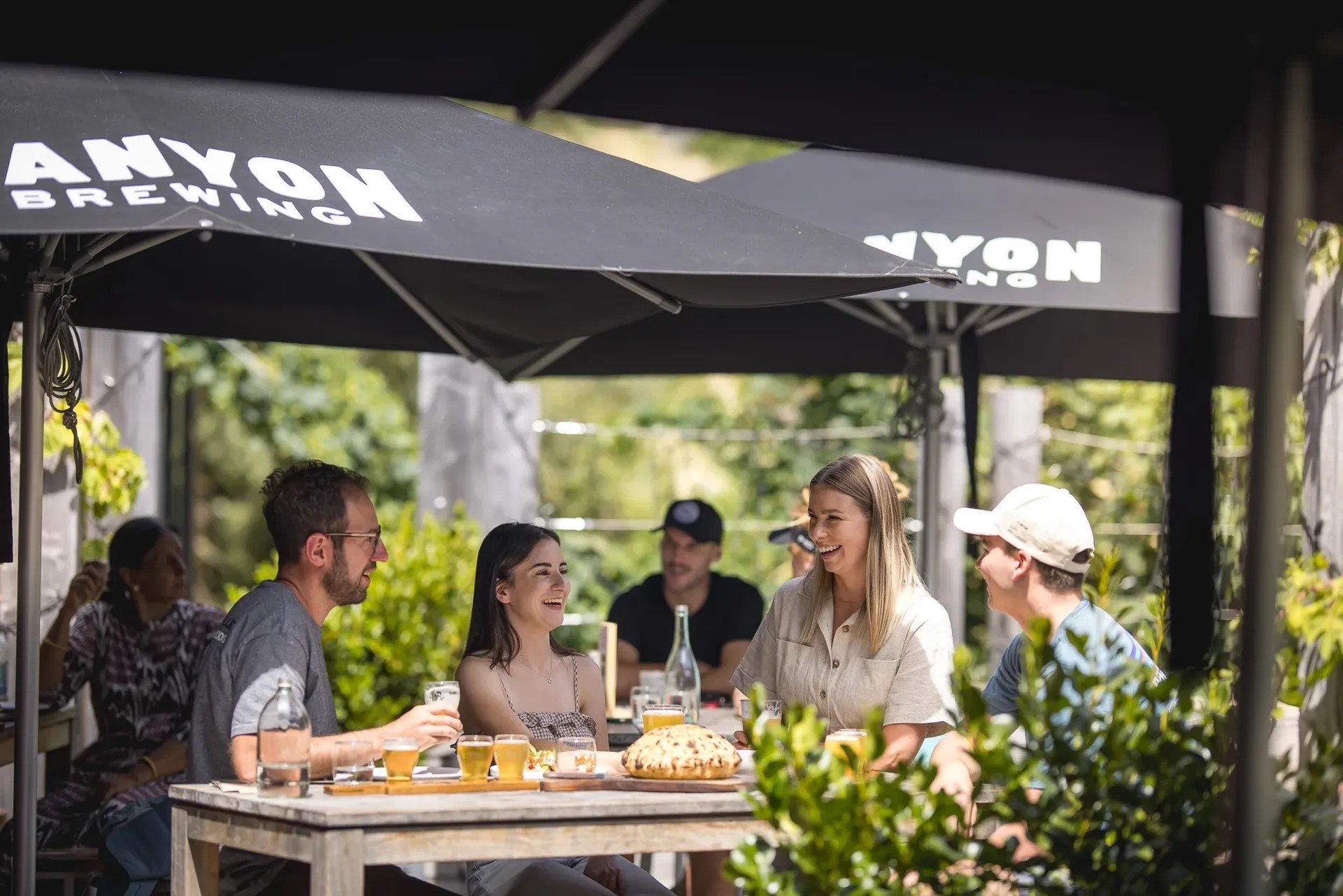 Casual outdoor dining at Canyon Brewing with patrons sharing drinks and food under black branded gazebo.
