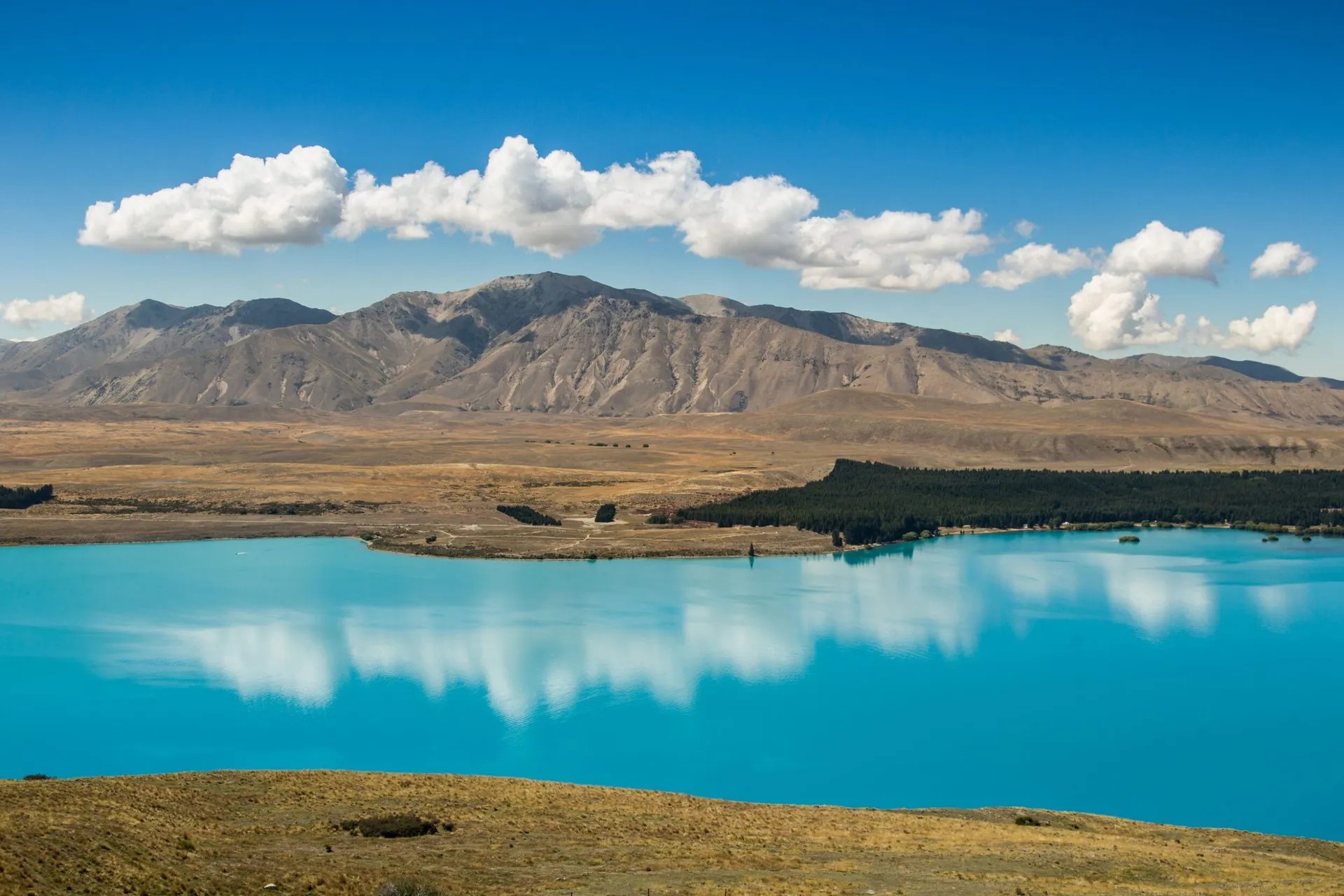 Famous Lake Tekapo with distinctive blue glacial waters, golden hills and Southern Alps mountain backdrop.