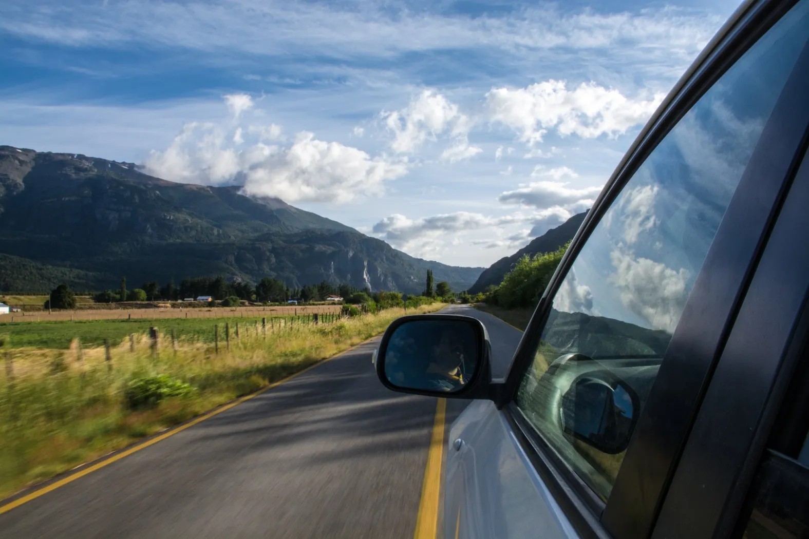 Road trip view from car showing scenic countryside with mountain ranges and rural farmland ahead.