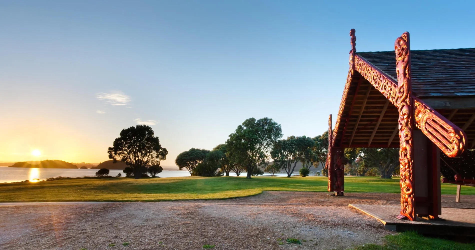 Waka shelter at the Waitangi Treaty Grounds with sun rising in the distance.