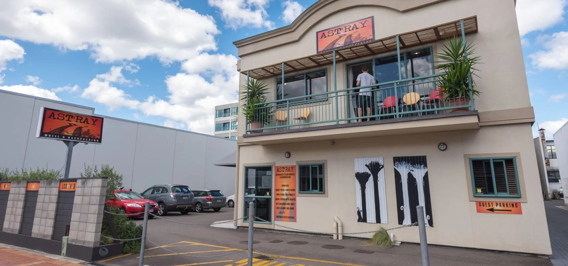 Modern backpacker accommodation exterior featuring artistic wall mural, upper level balcony and on-site car parking.