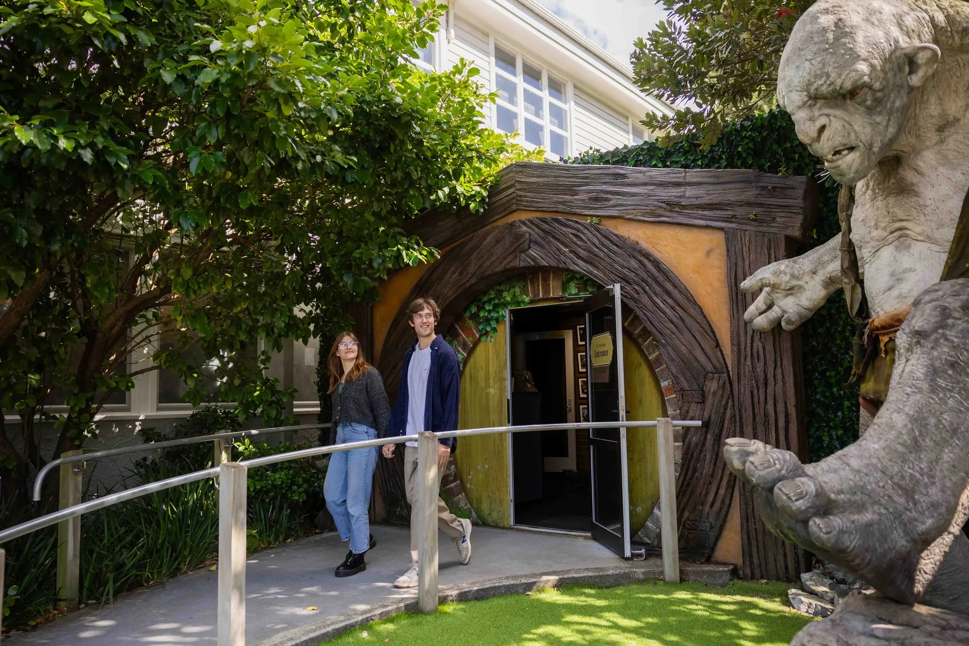 Man and woman walking out of the Weta Workshop Cave Tour entrance, looking at a large Lord of the Rings statue.