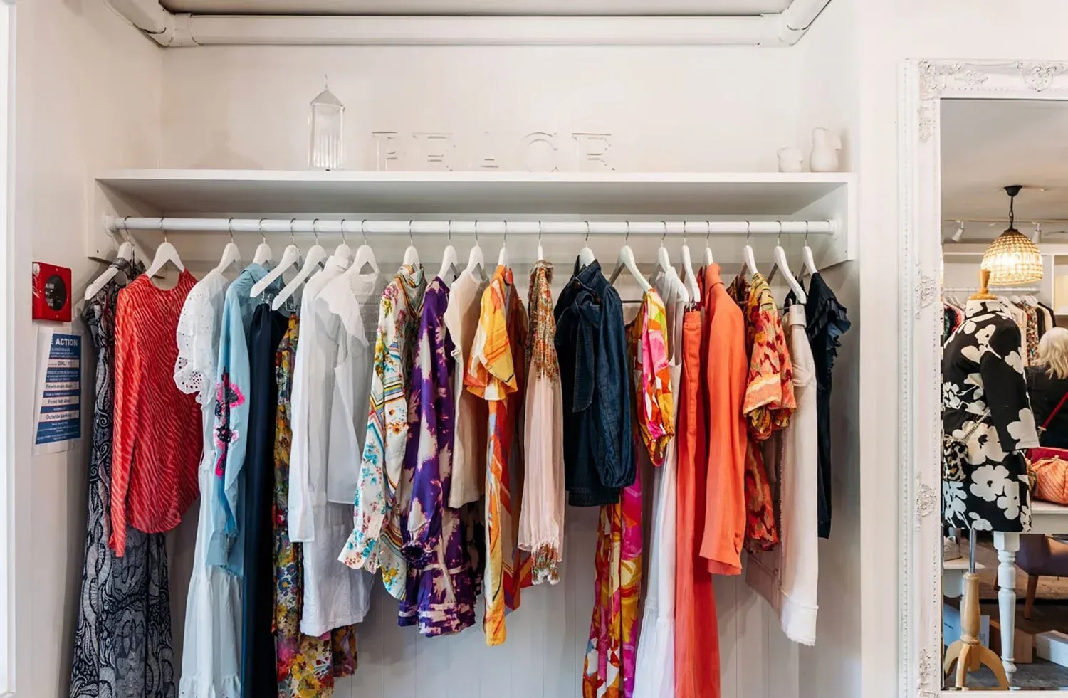 Rack of colourful clothes and a mirror in a clothing consignment store.