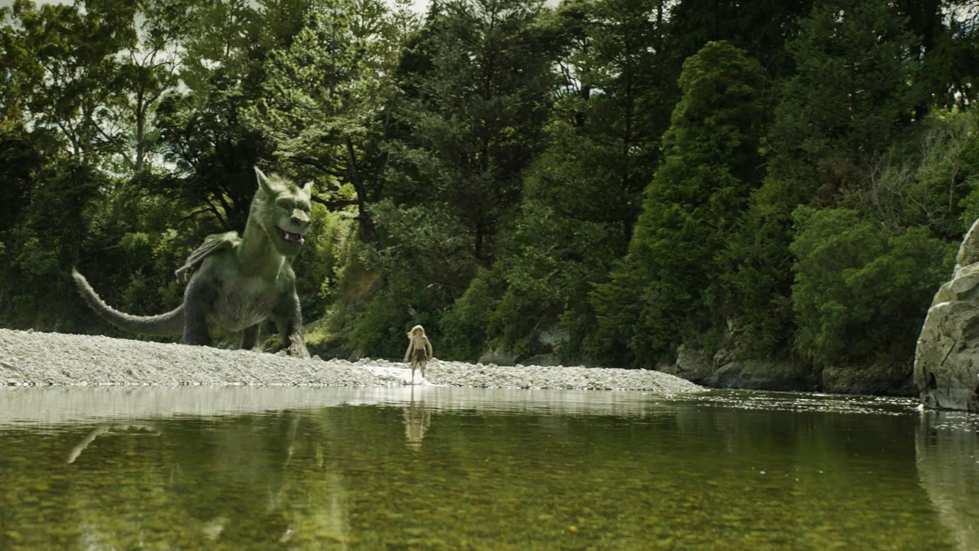 Screenshot of the 2016 Pete's Dragon film, featuring Pete and the dragon standing by a body of water in a forest.