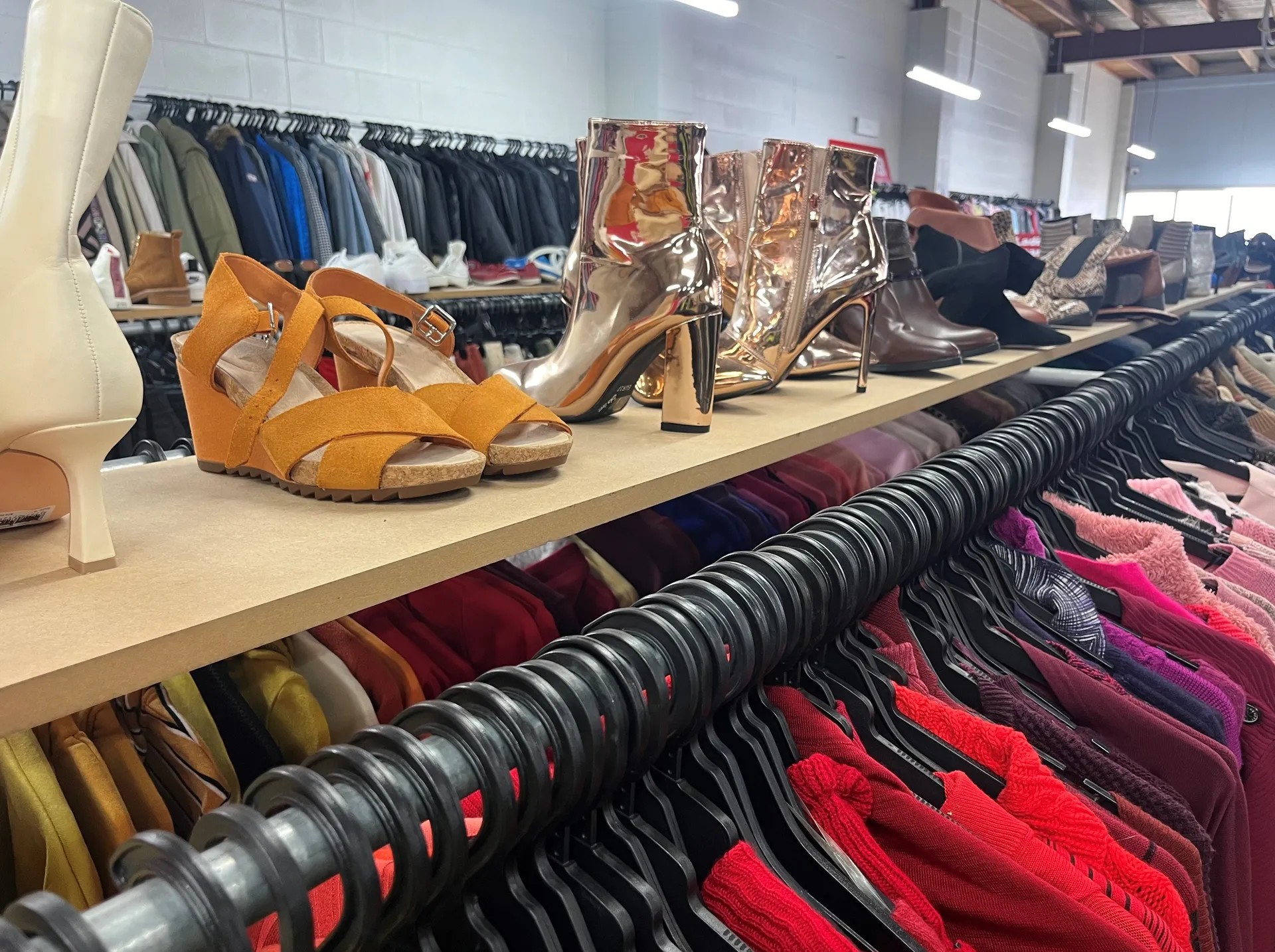Op shop rack with red-pink clothes and shoes on top.