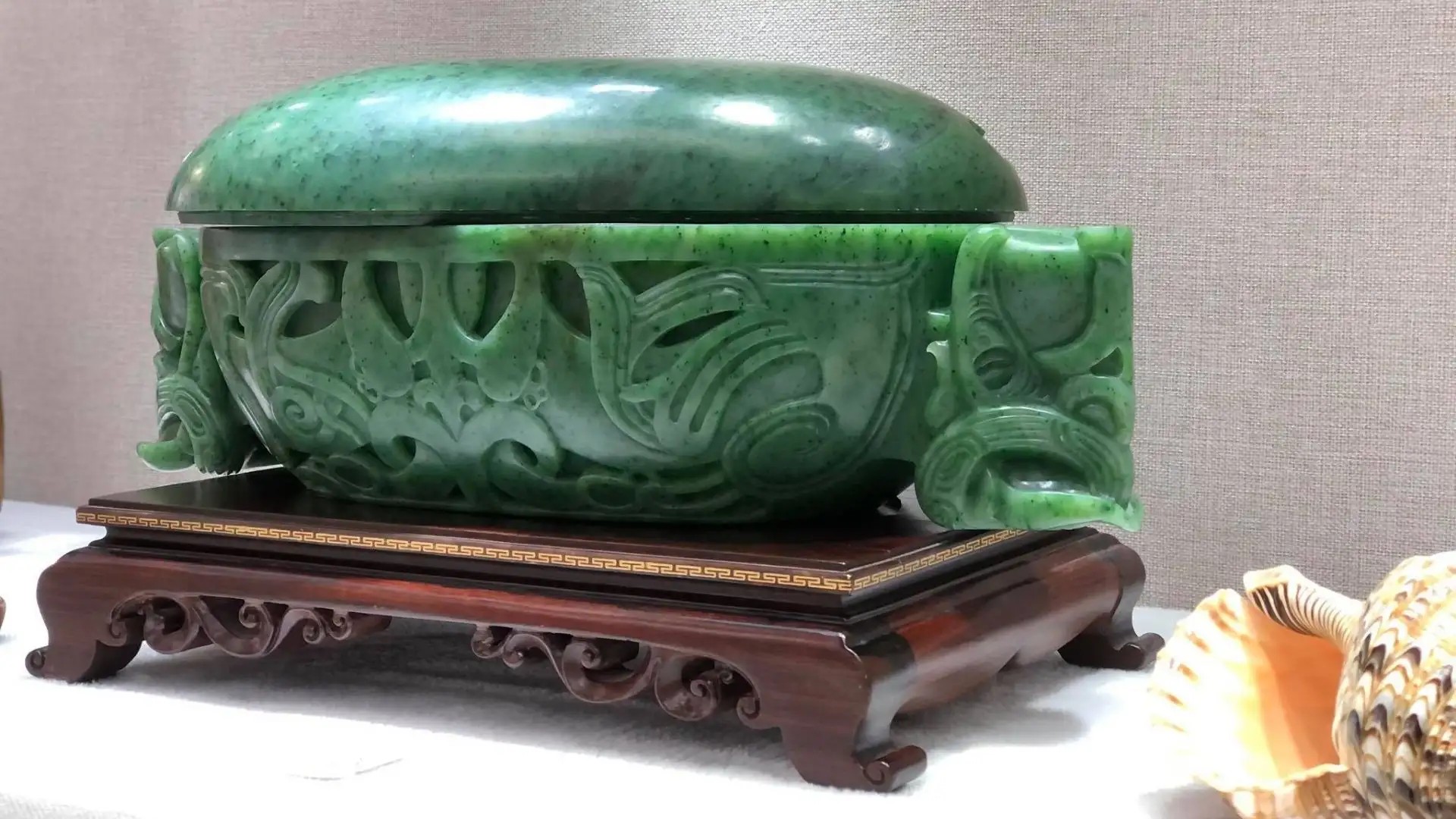 Jade bowl sculpture incorporating Maori design elements resting on a wooden Chinese display board.