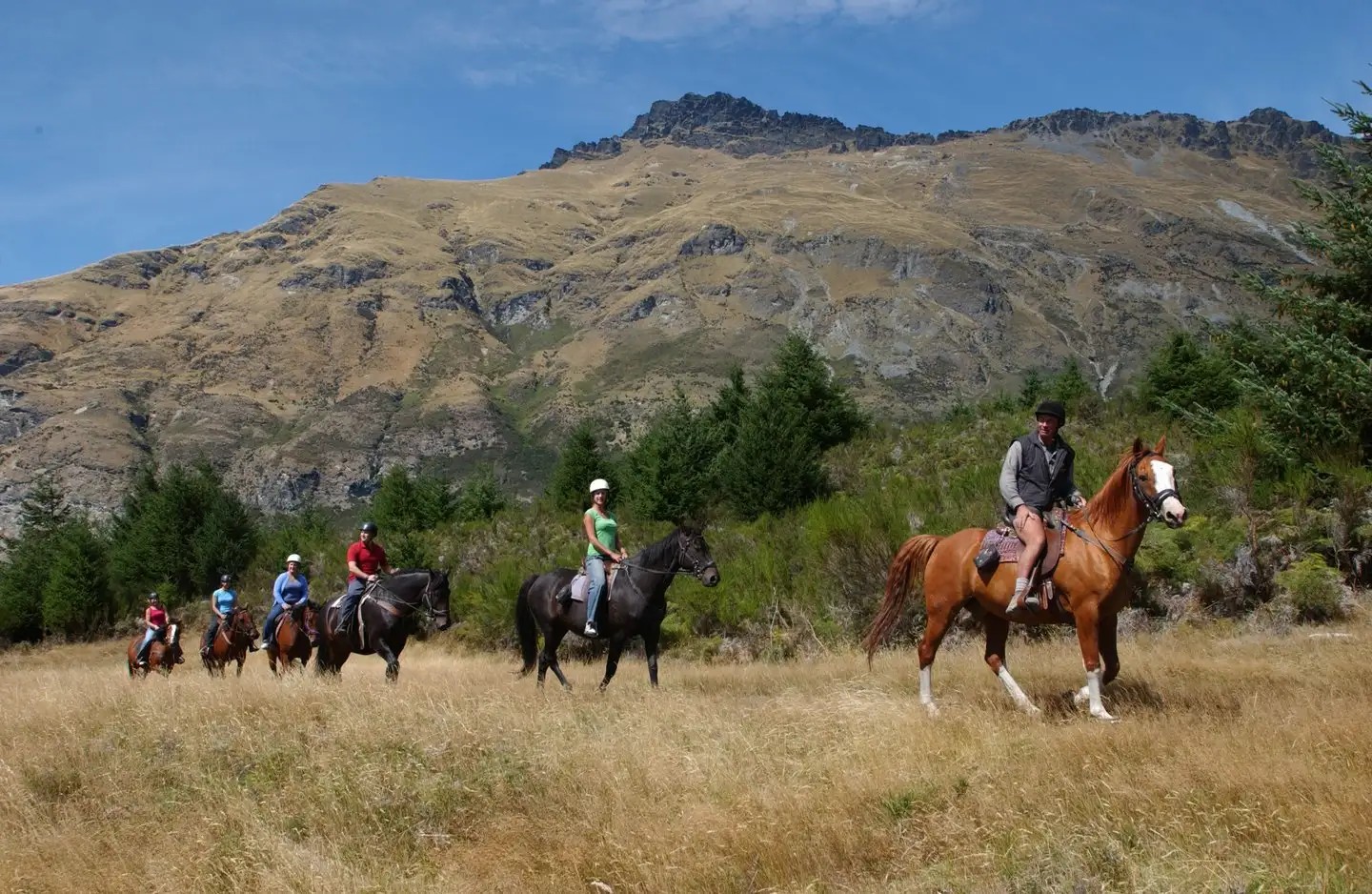 6 people on horseback riding in the mountains.