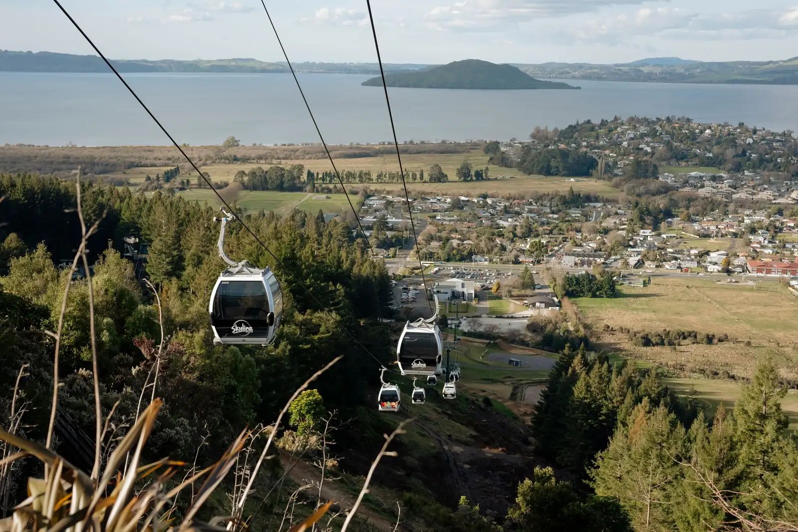 Skyline Gondola going up the mountain with a view of Lake Rotorua and Rotorua city in the distance.