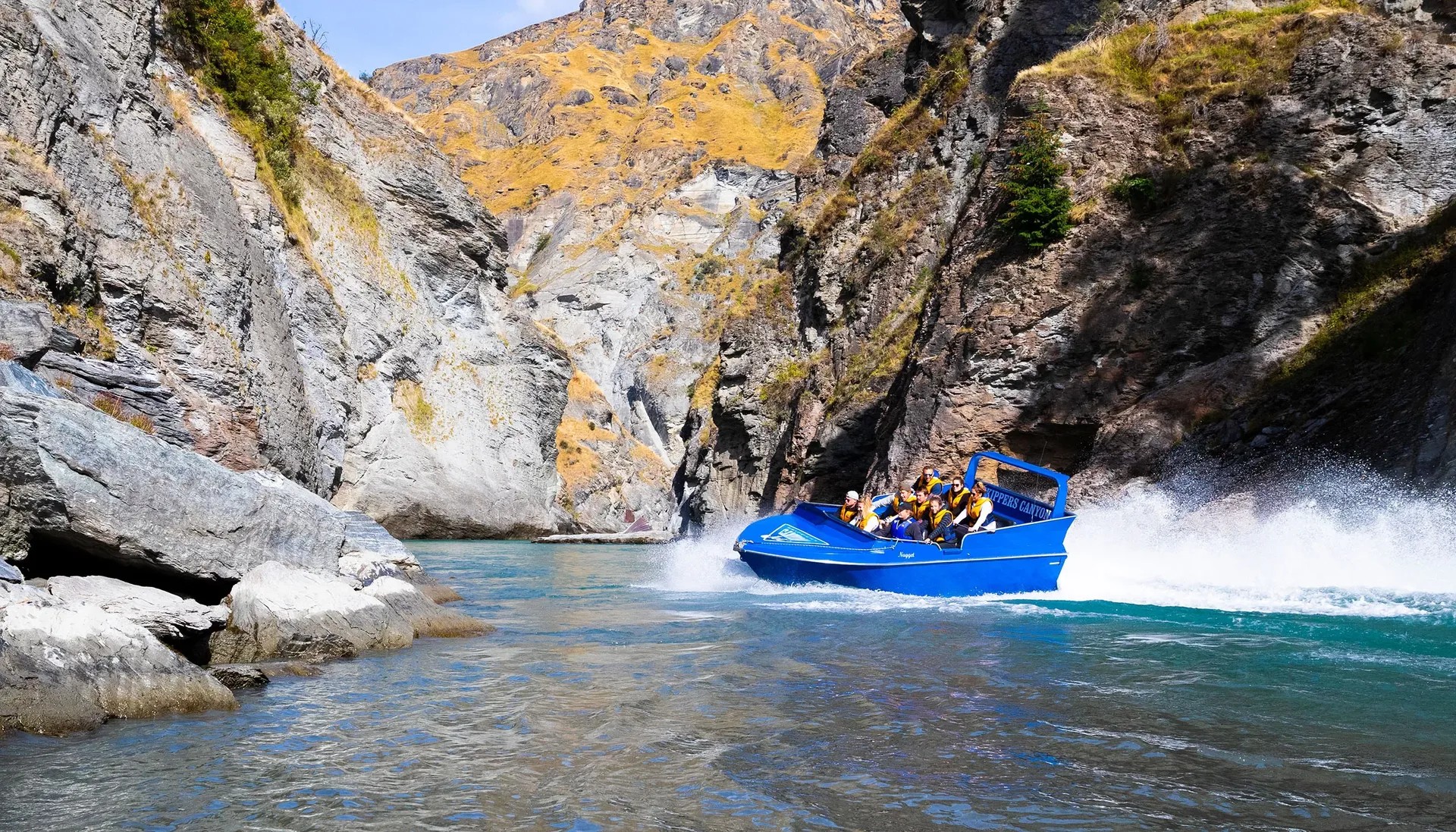 Jetboat riding through clear river waters and surrounded by rocky cliff faces.
